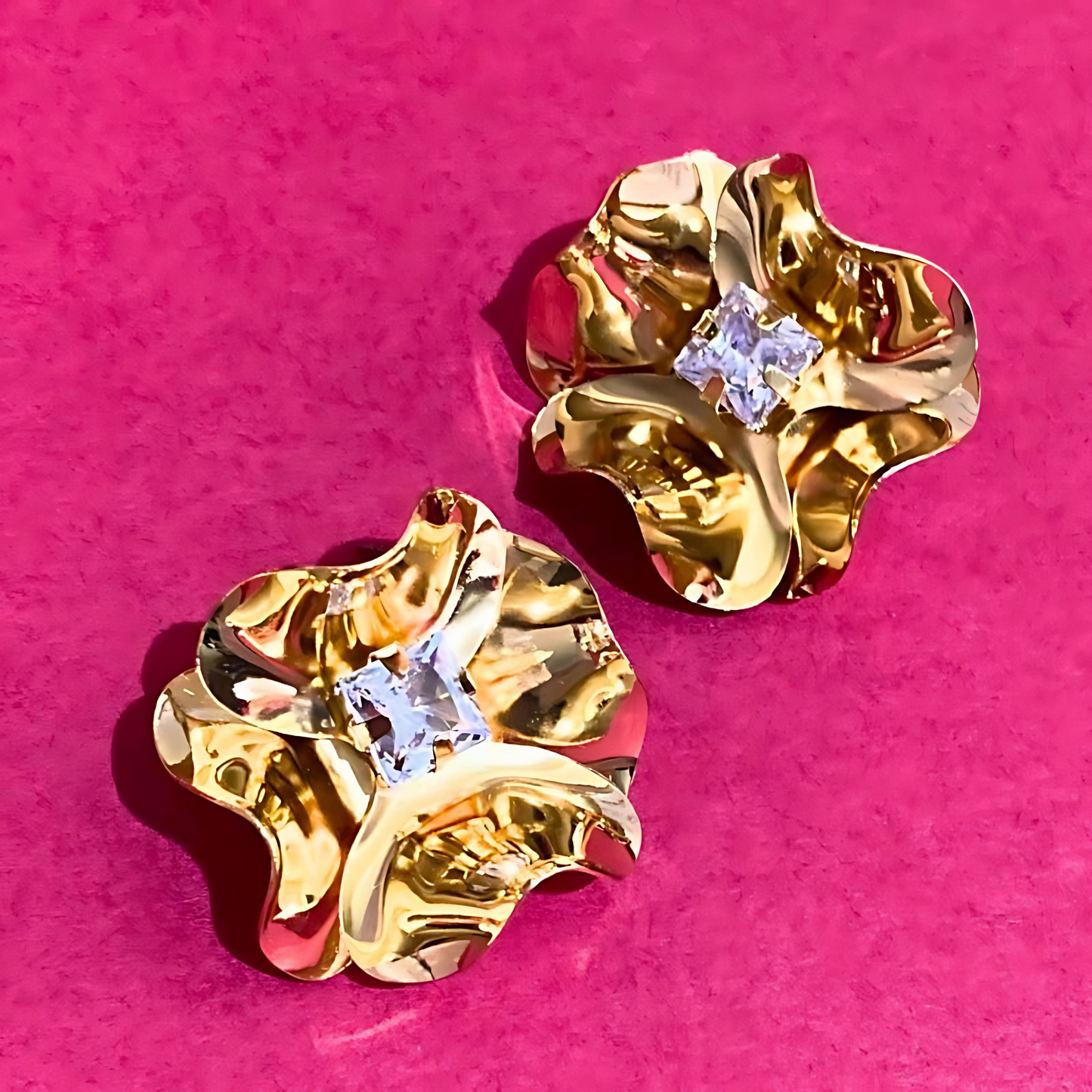 Gold earrings with clear gemstones on a pink background