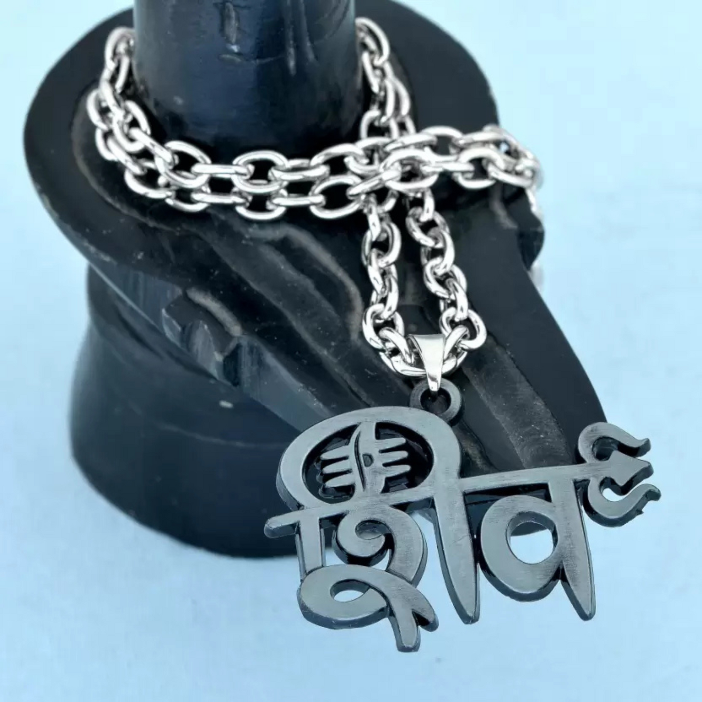 Silver chain necklace with a pendant on a black stand against a light blue background