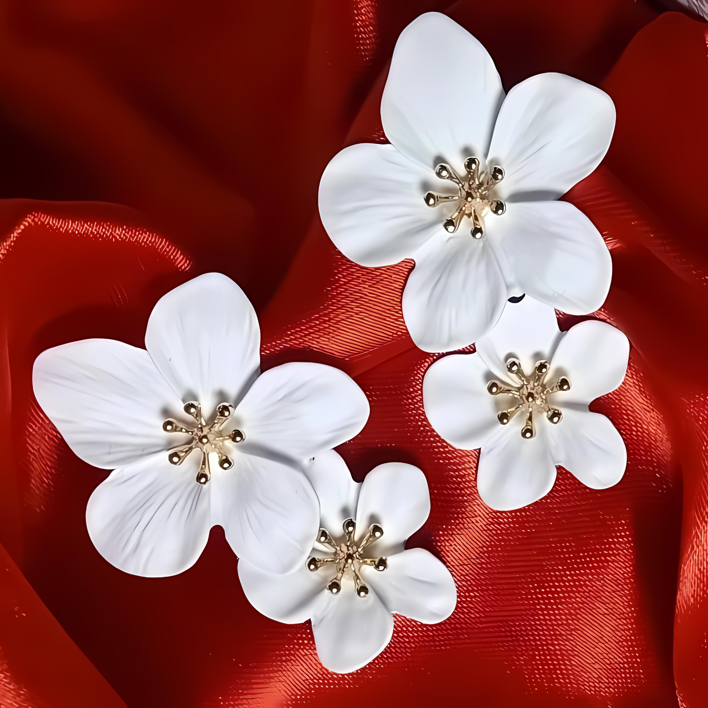 White floral earrings with gold centers on a red fabric background