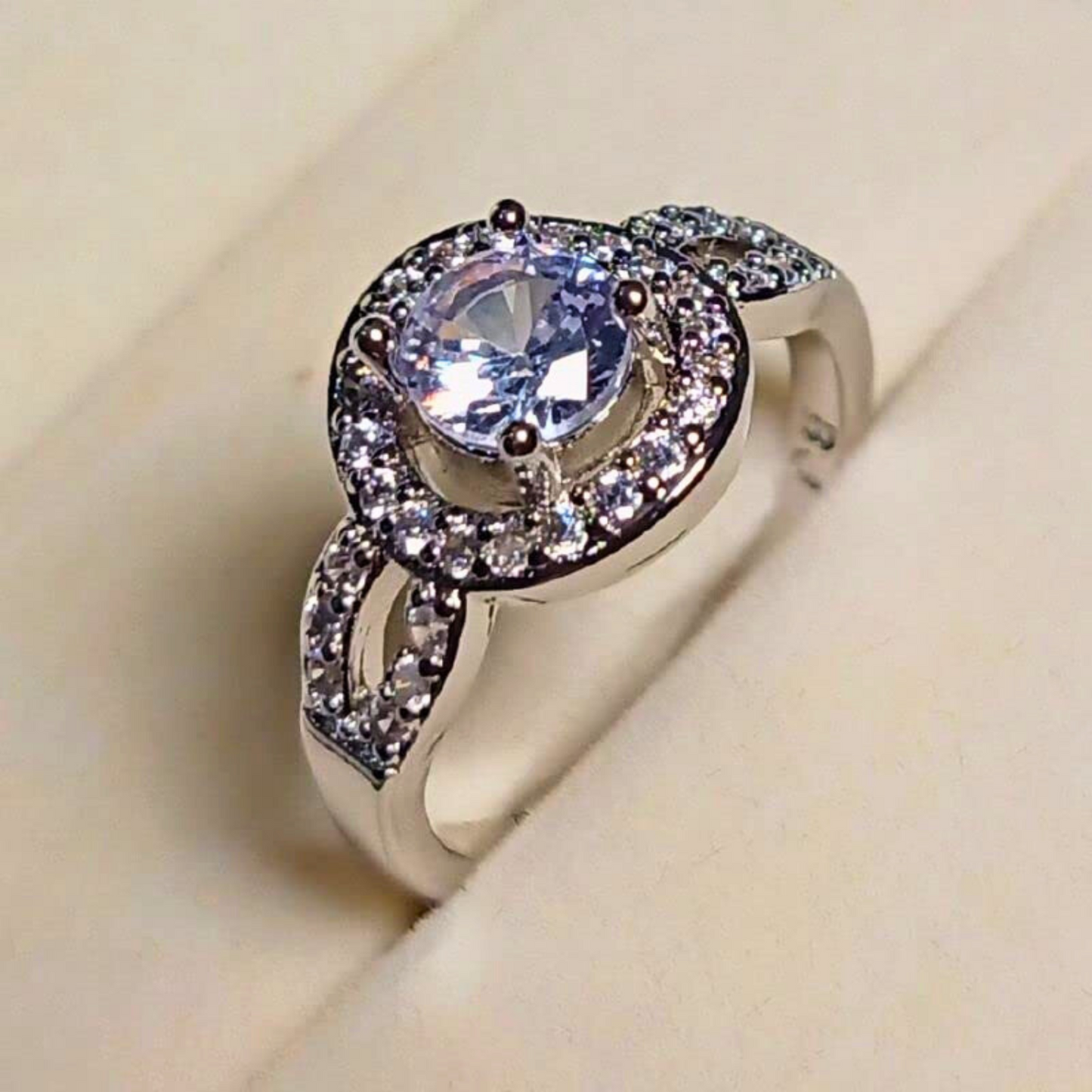 Silver ring with a large central gemstone and smaller stones on a beige background