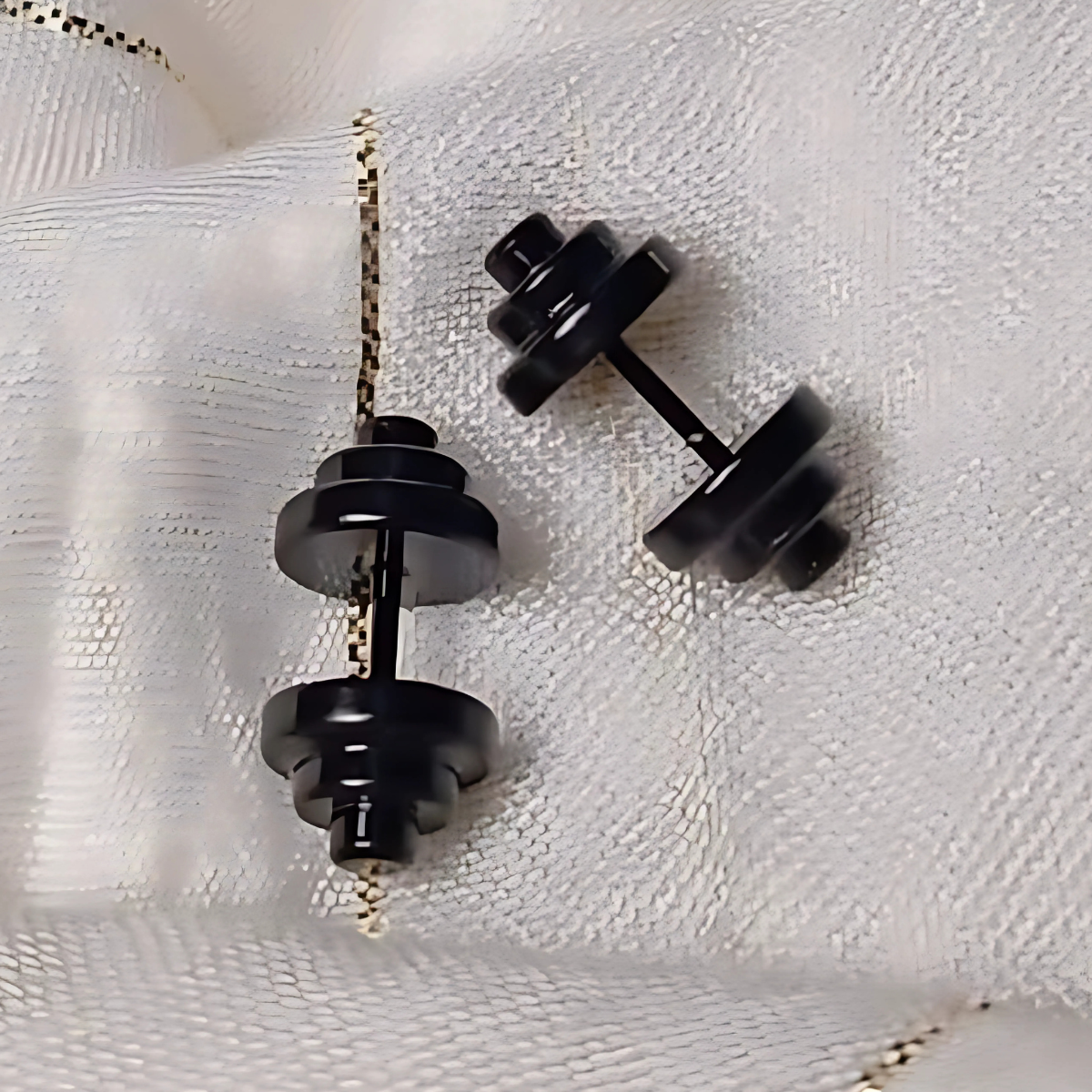 Black dumbbell-shaped earrings on a white textured background