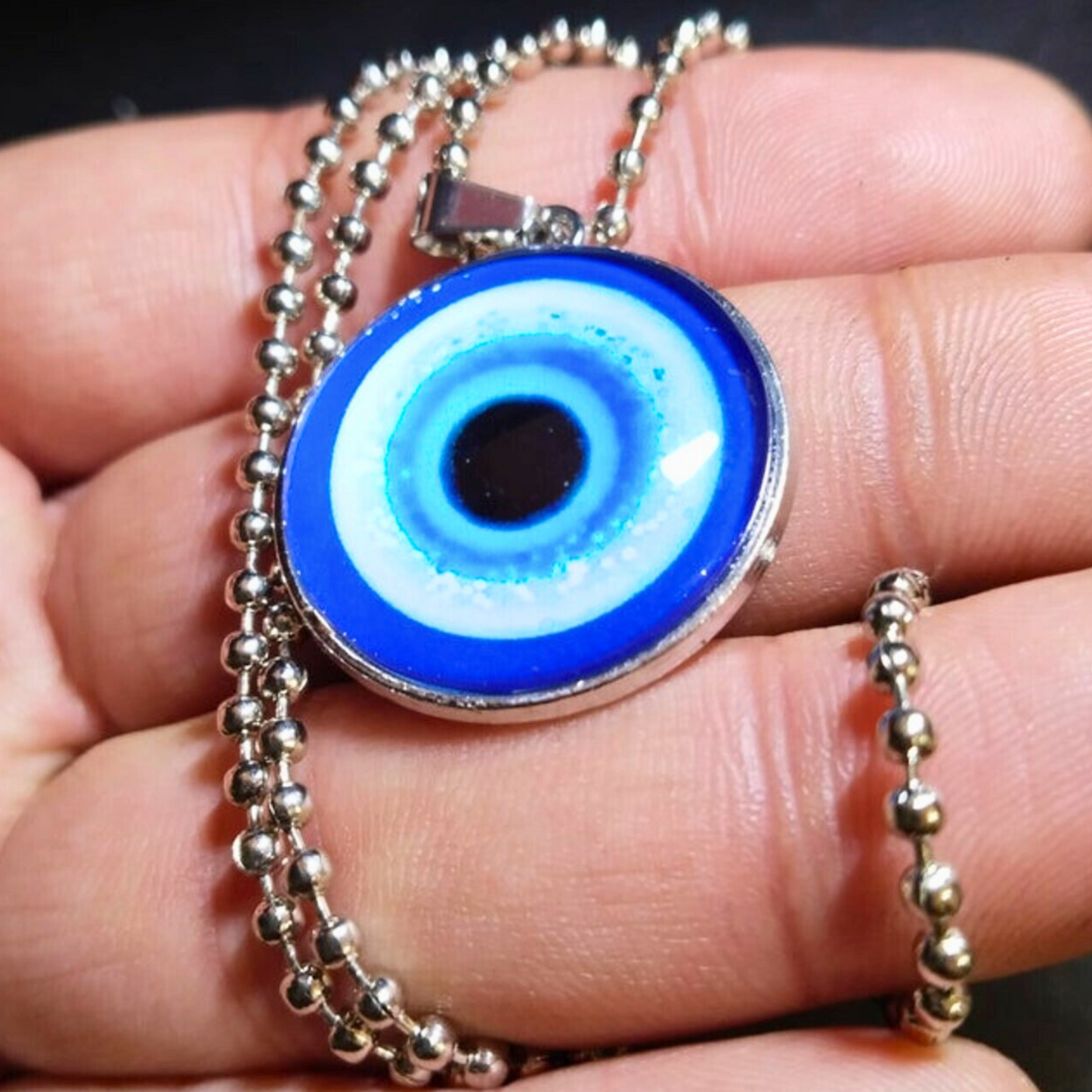 Blue evil eye pendant on a chain held between fingers