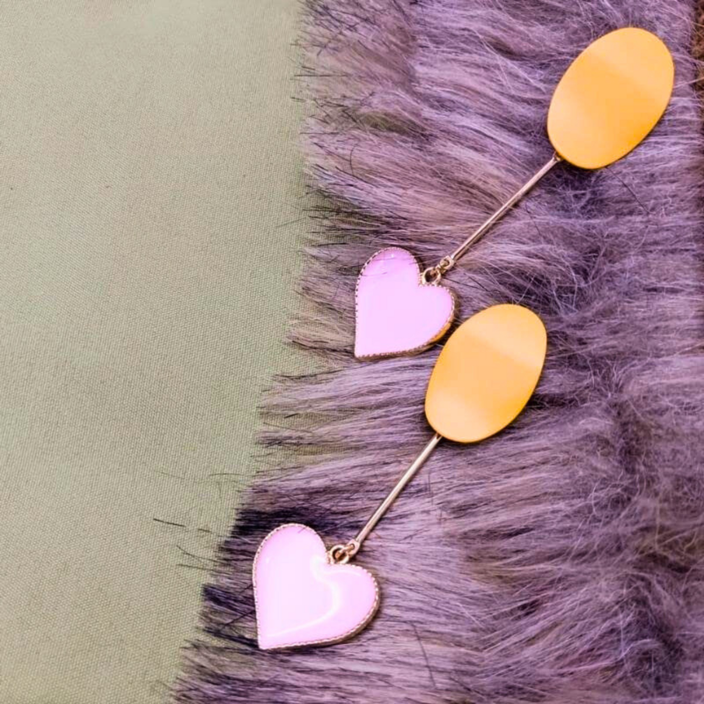 Pair of earrings with pink heart and yellow oval charms on a textured surface.