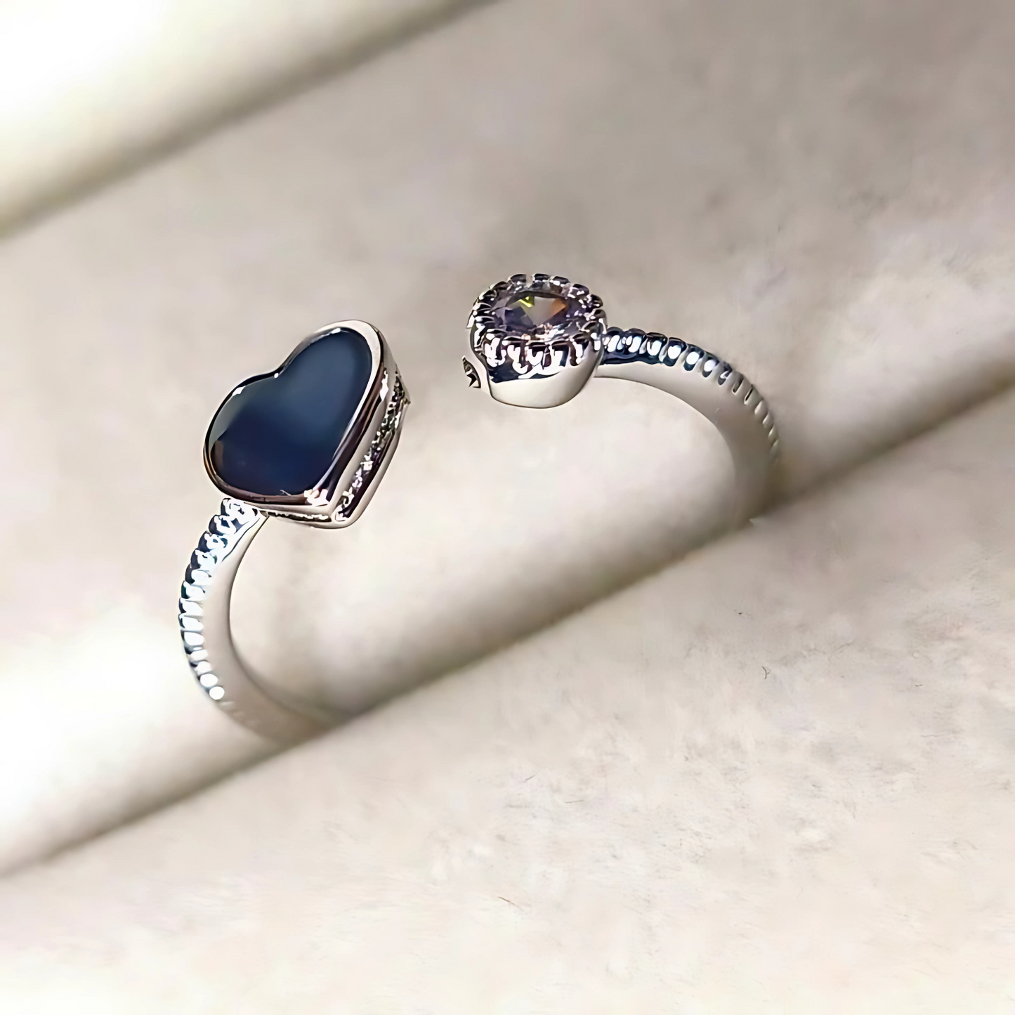Two silver rings with blue and clear gemstones on a light beige surface