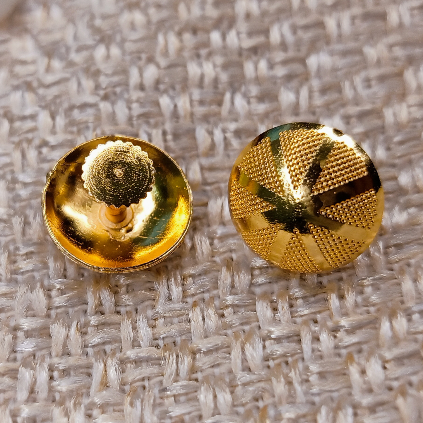 Pair of gold textured buttons stud earring on a textured fabric background