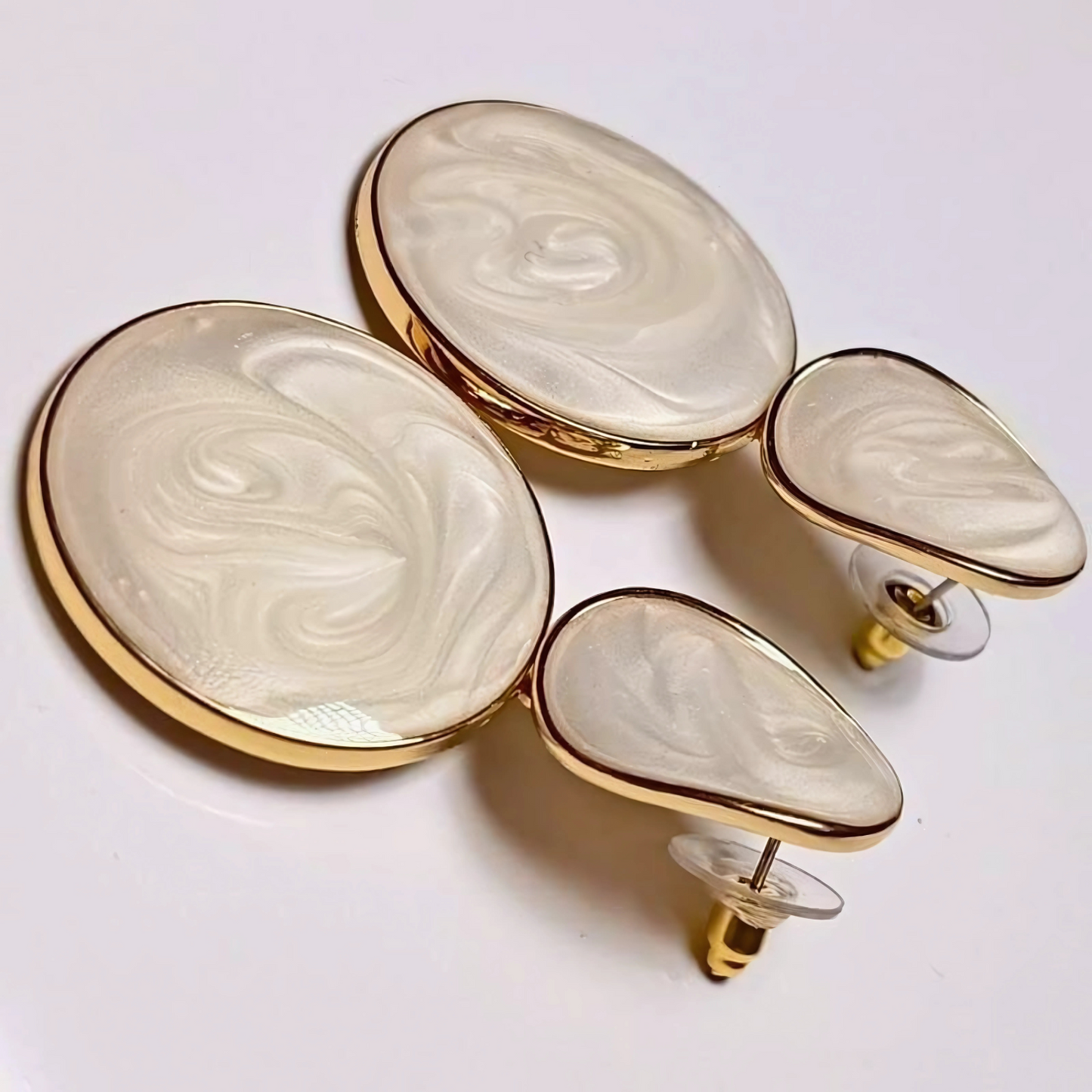 Set of gold and white marbled earrings on a light background