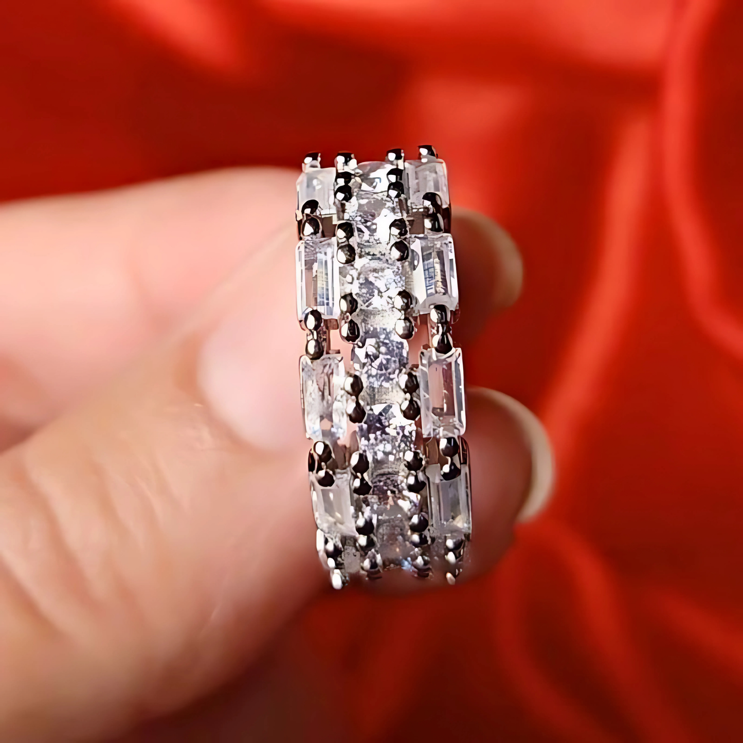 Silver ring with gemstones held between fingers against a red fabric background