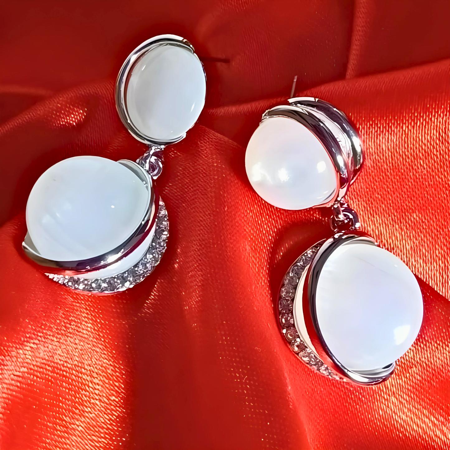 Silver earrings with white stones on a red fabric background