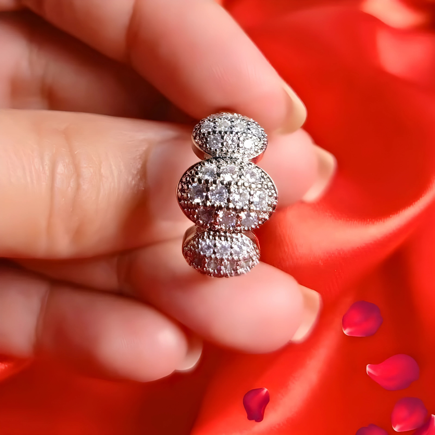 Silver earrings held between fingers against a red background with rose petals