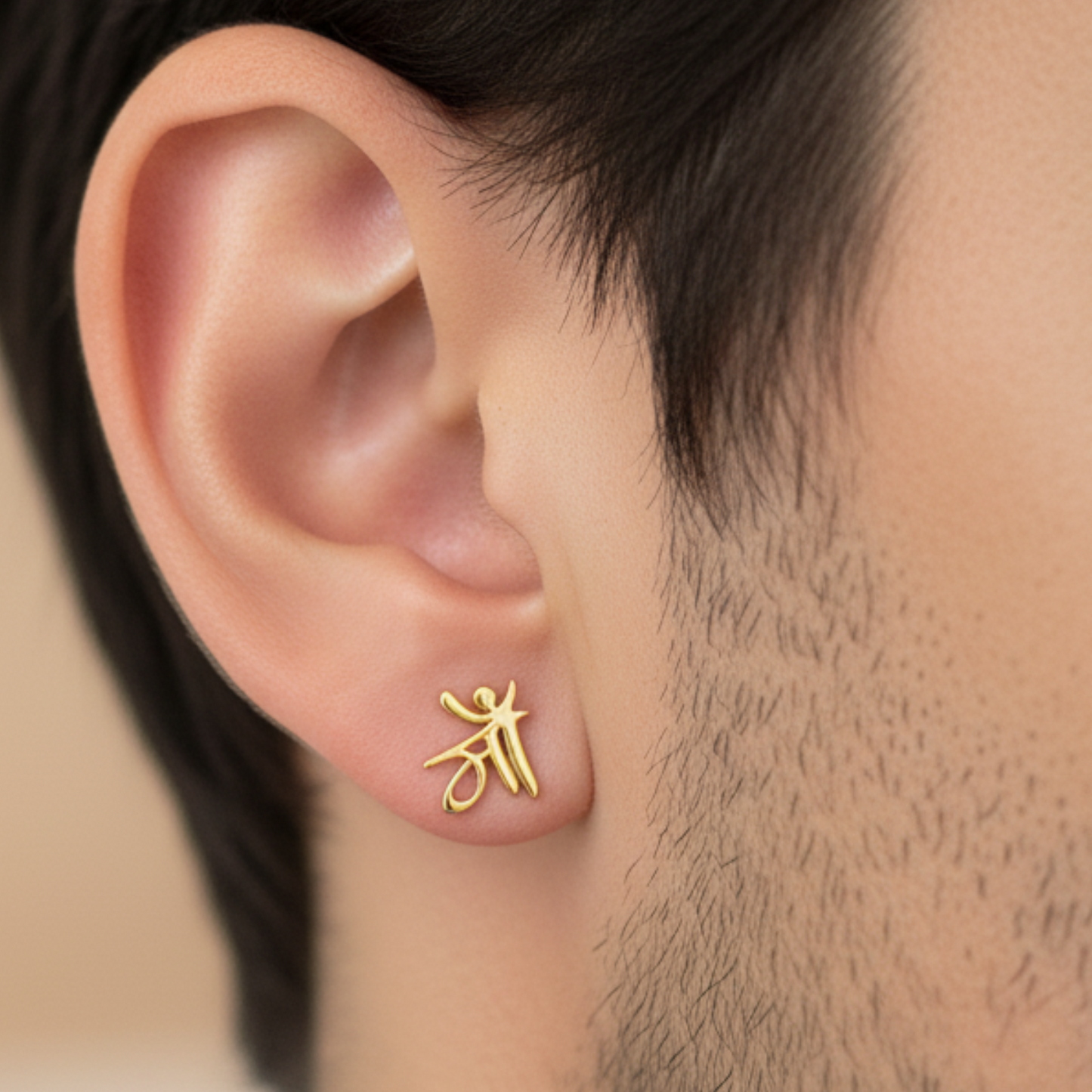 Gold earring worn on a person's ear with a neutral background