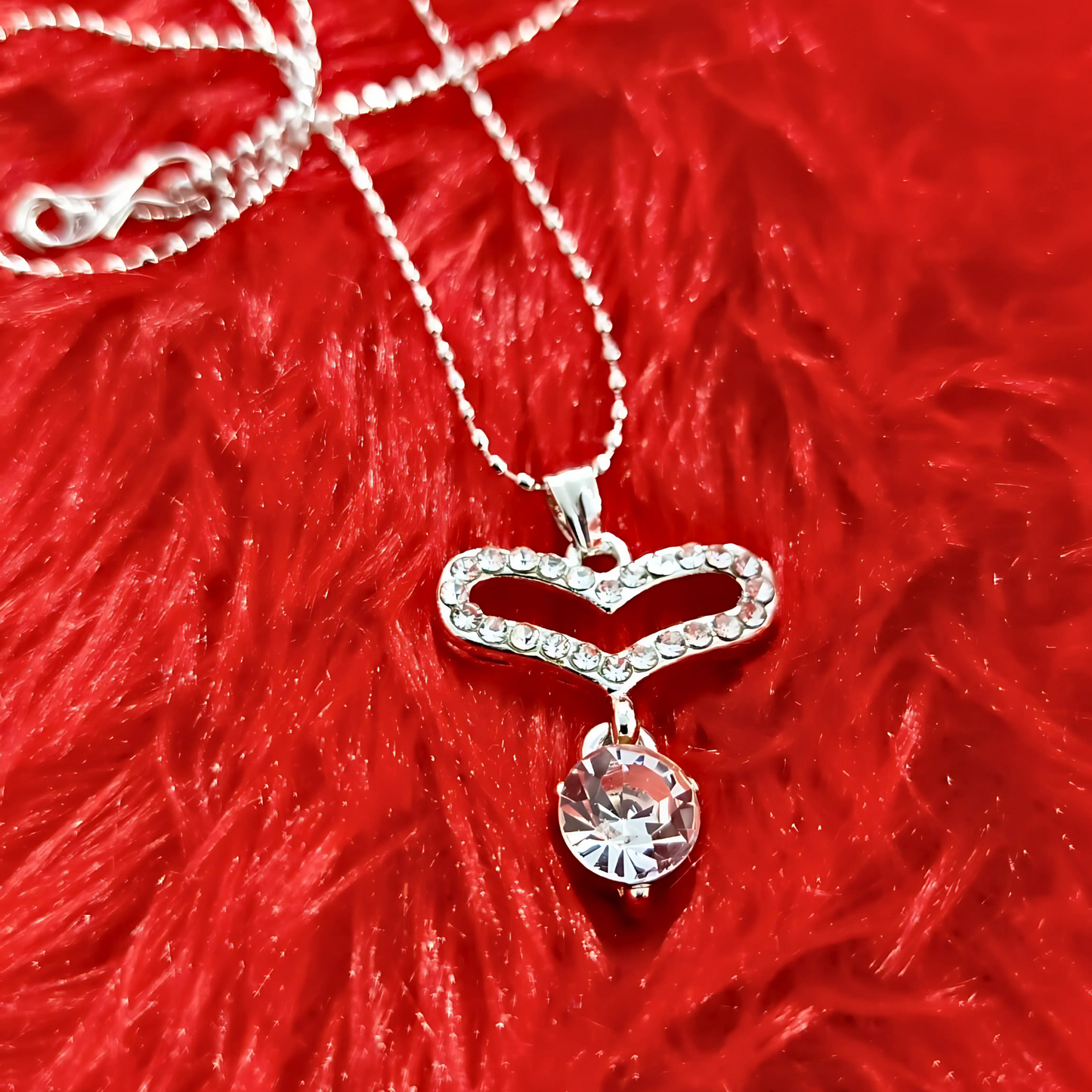 Silver necklace with a heart-shaped pendant on a red textured background