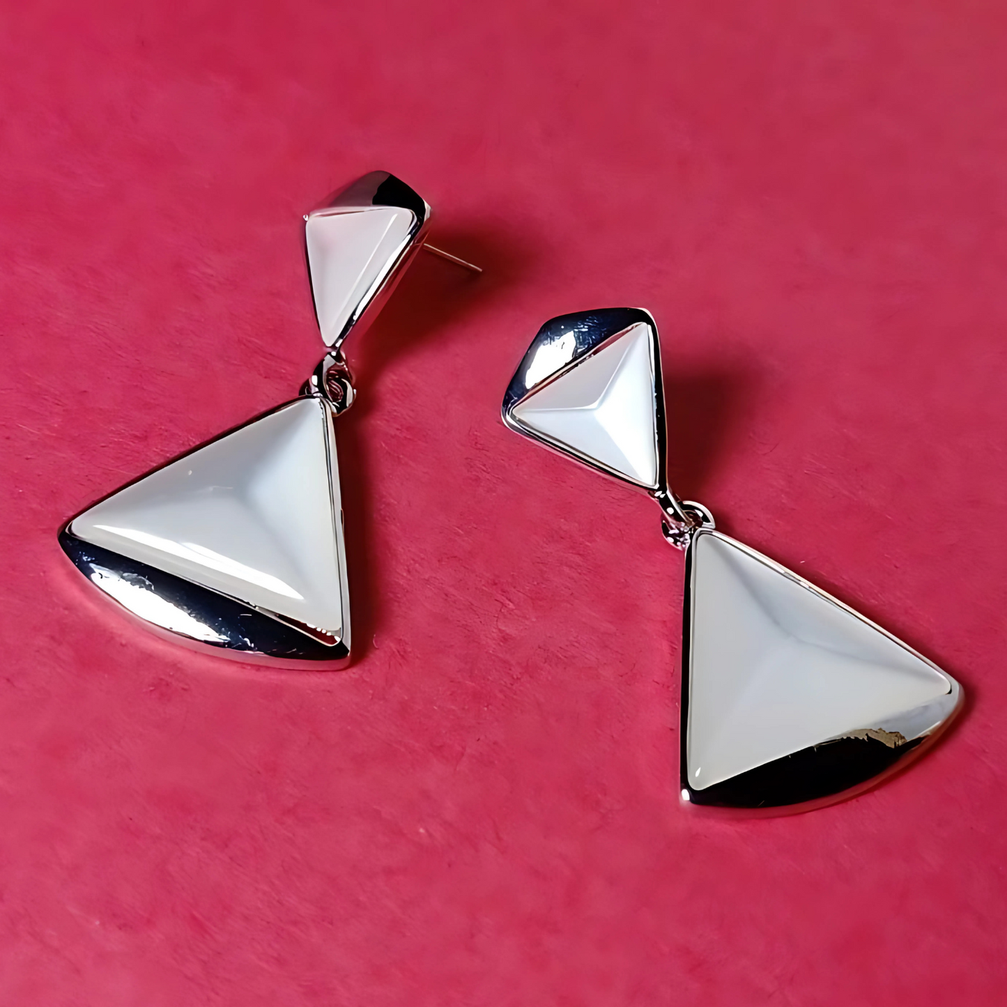 Pair of silver triangle earrings on a pink background