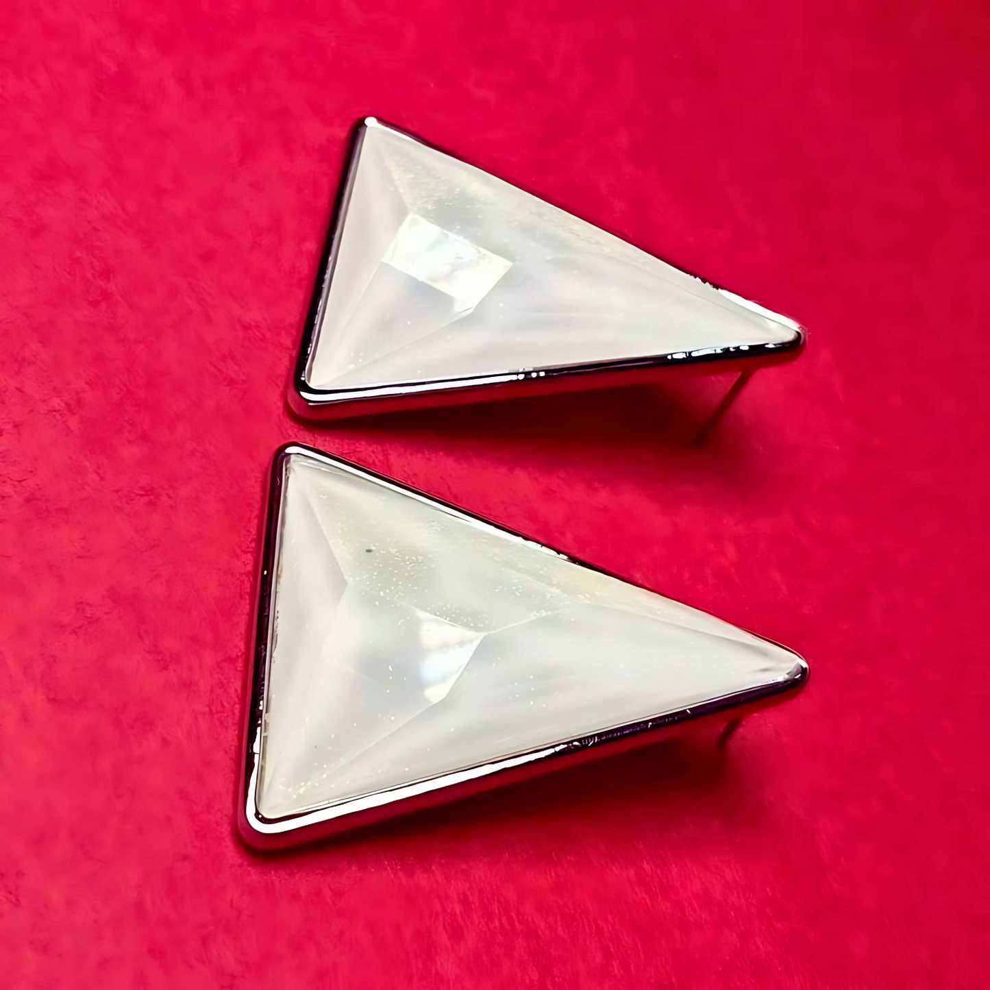 Two triangular earrings with a reflective surface on a red background