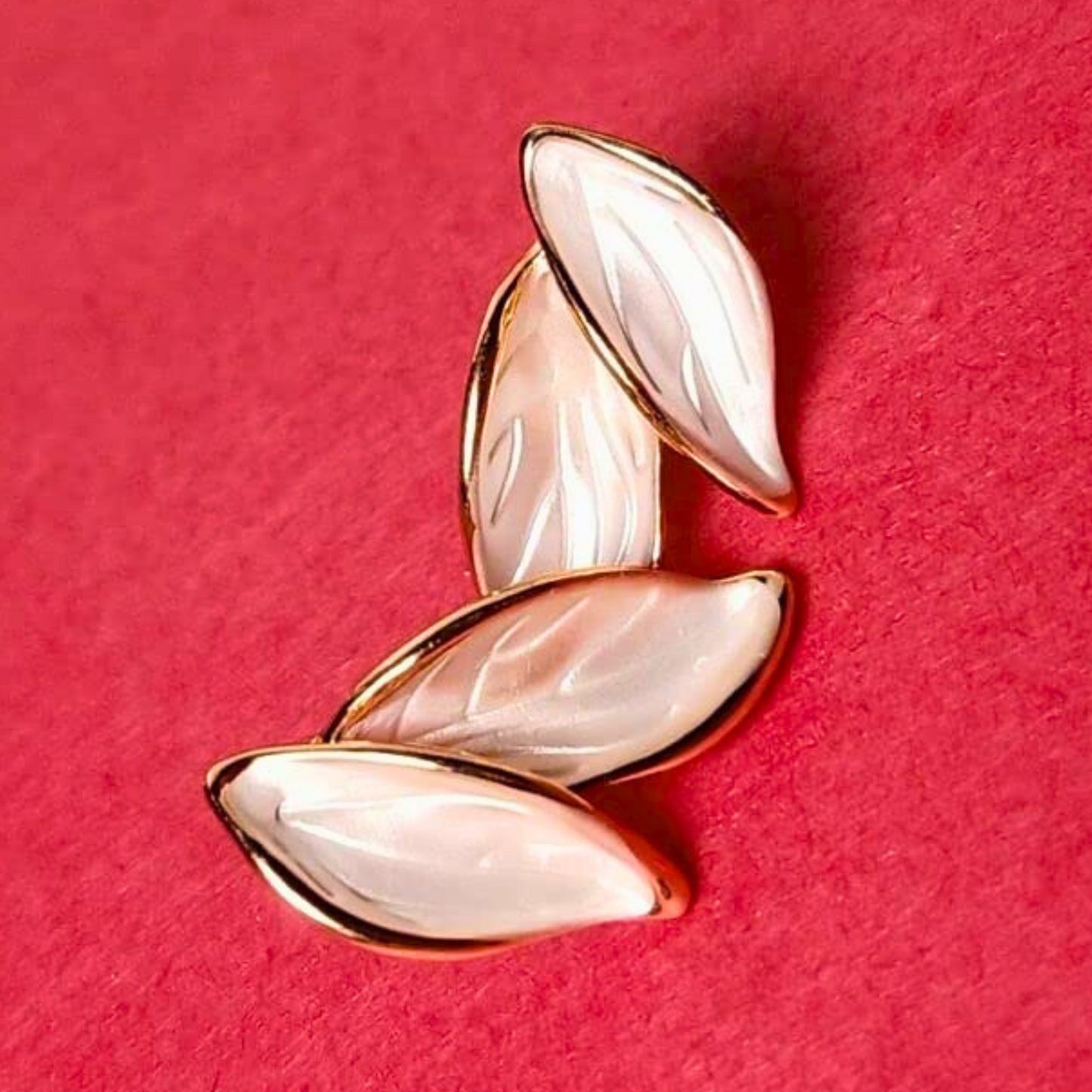 Pair of gold and beige leaf-shaped earrings on a red background