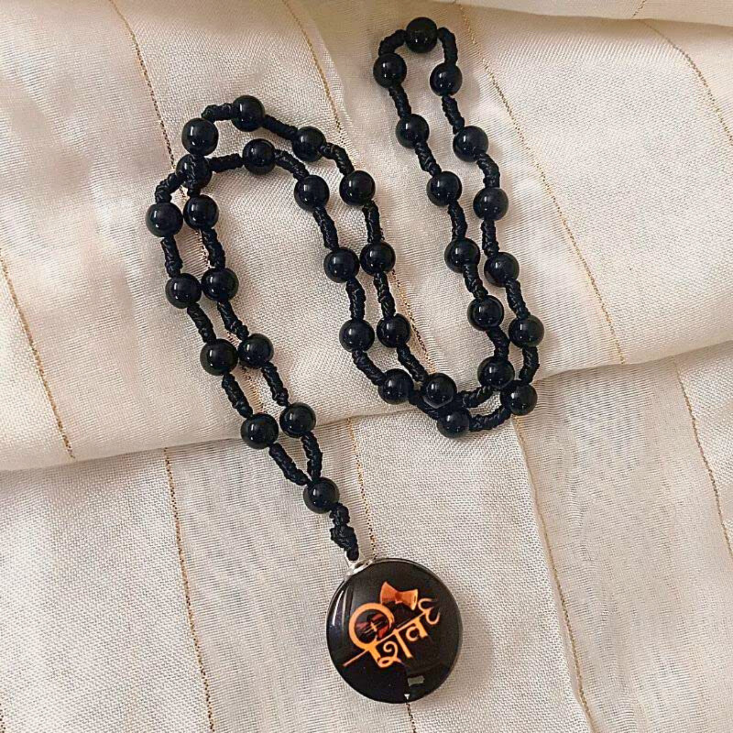 Black beaded necklace with a pendant on a beige fabric background