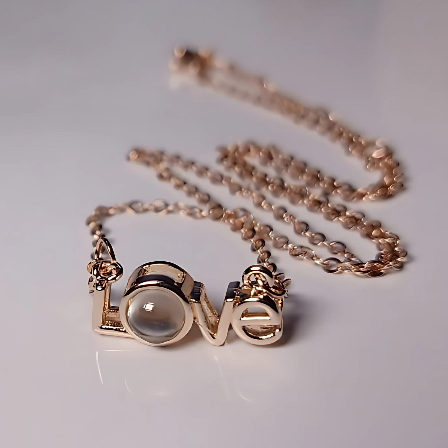Rose gold necklace with 'love' pendant on a light gray background