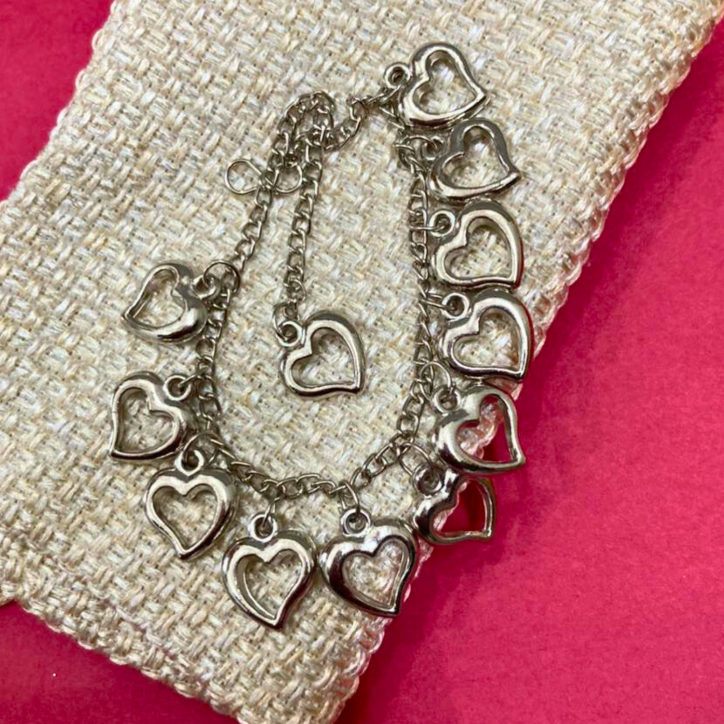Silver heart-shaped bracelet on a textured surface with a pink background