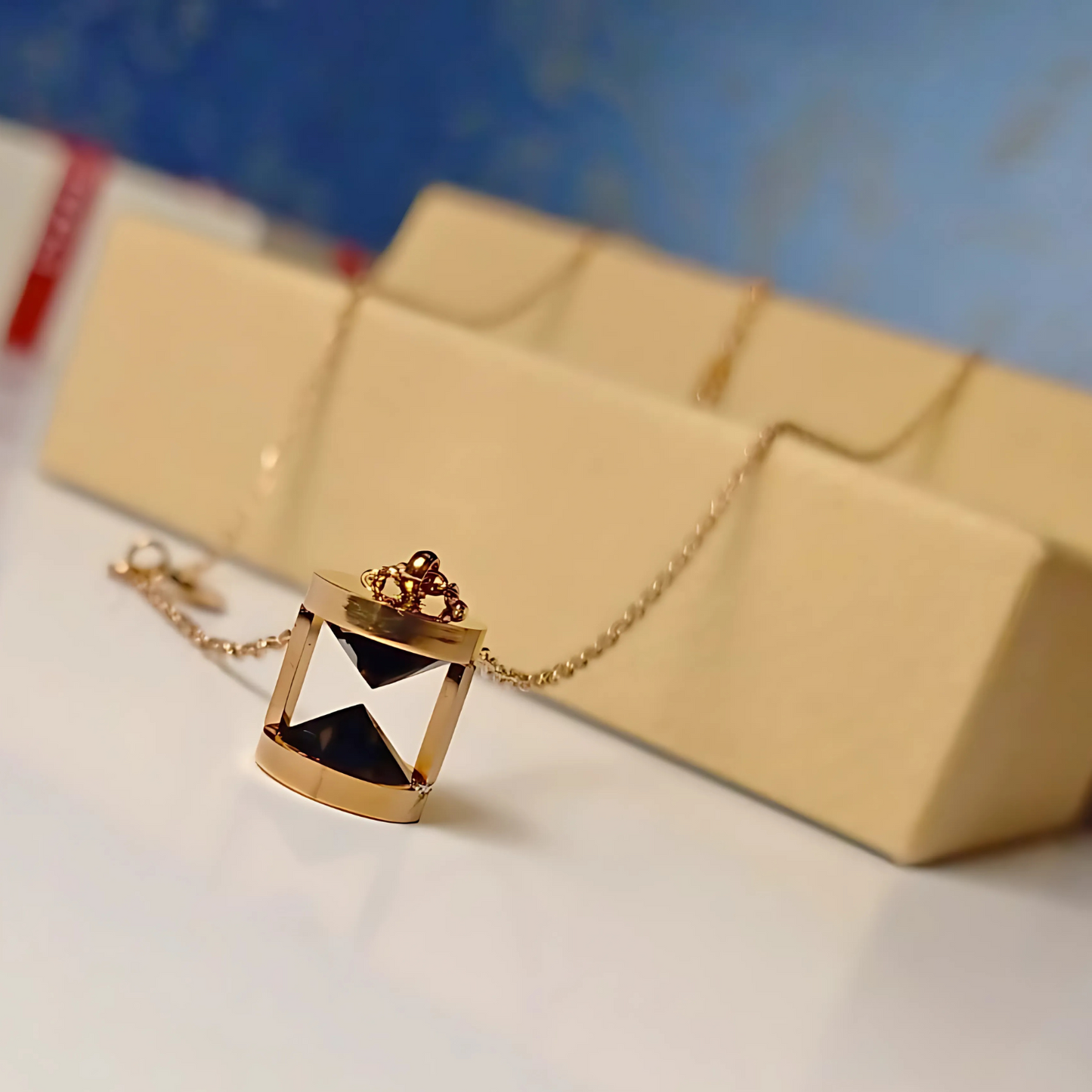 Gold necklace with a pendant on a white surface with a beige box in the background