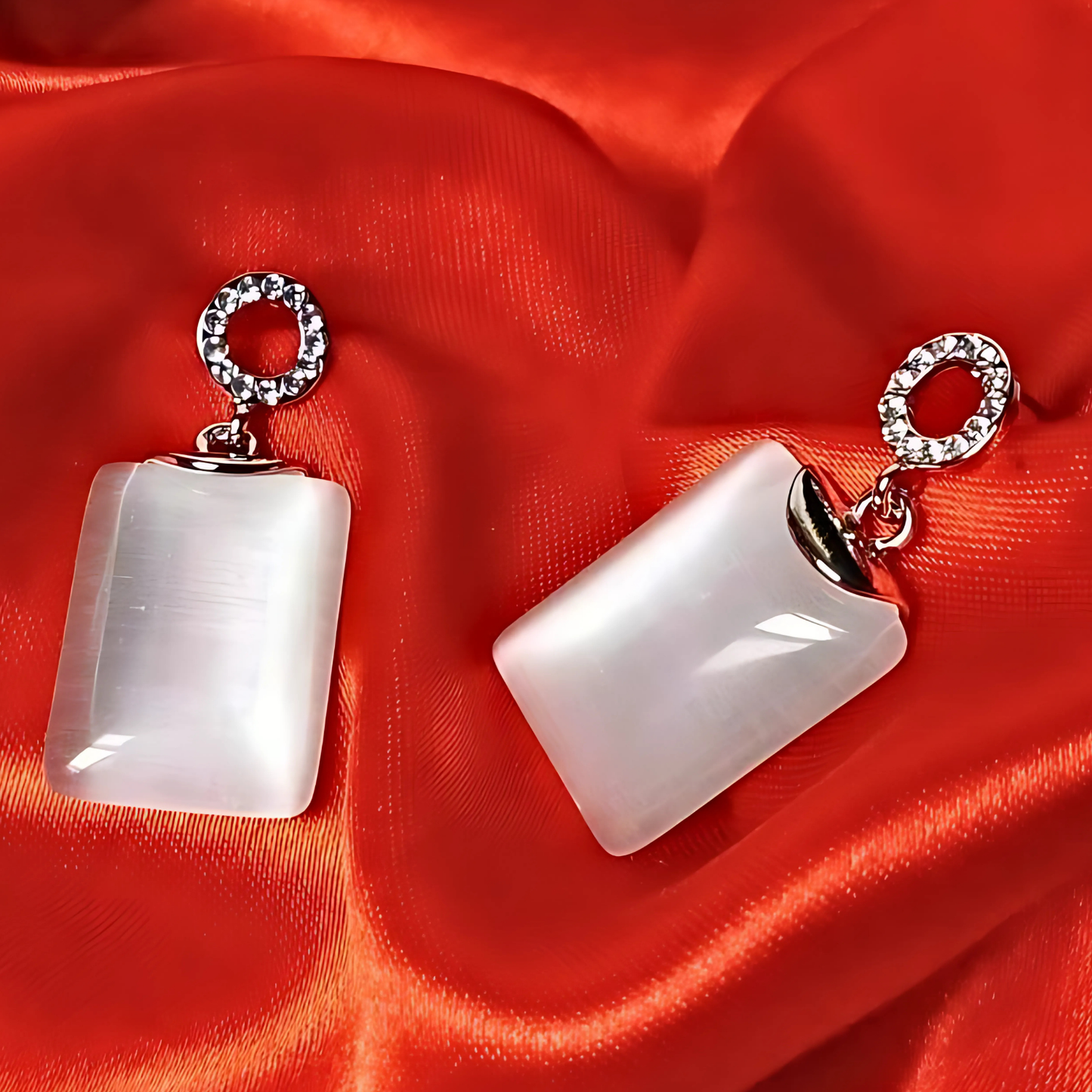 Pair of earrings with white stones and silver loops on a red fabric background