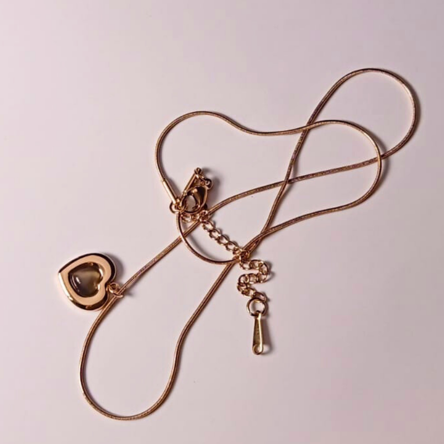 Gold necklace with a heart-shaped pendant on a light pink background