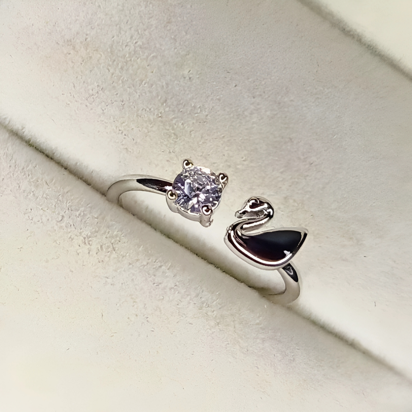 Silver ring with a diamond and a swan design on a light beige background