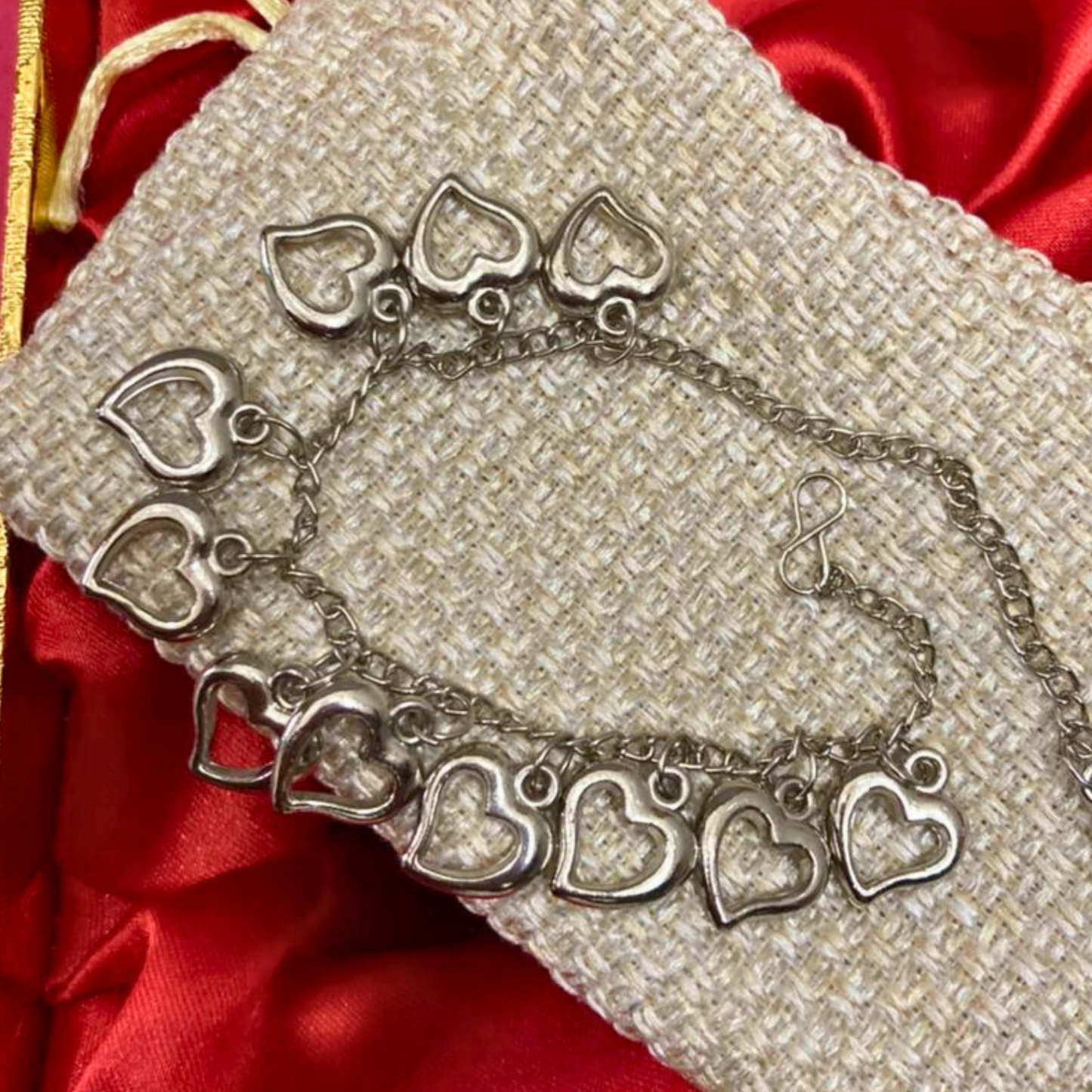 Silver bracelet with heart-shaped charms on a textured beige surface with red fabric background