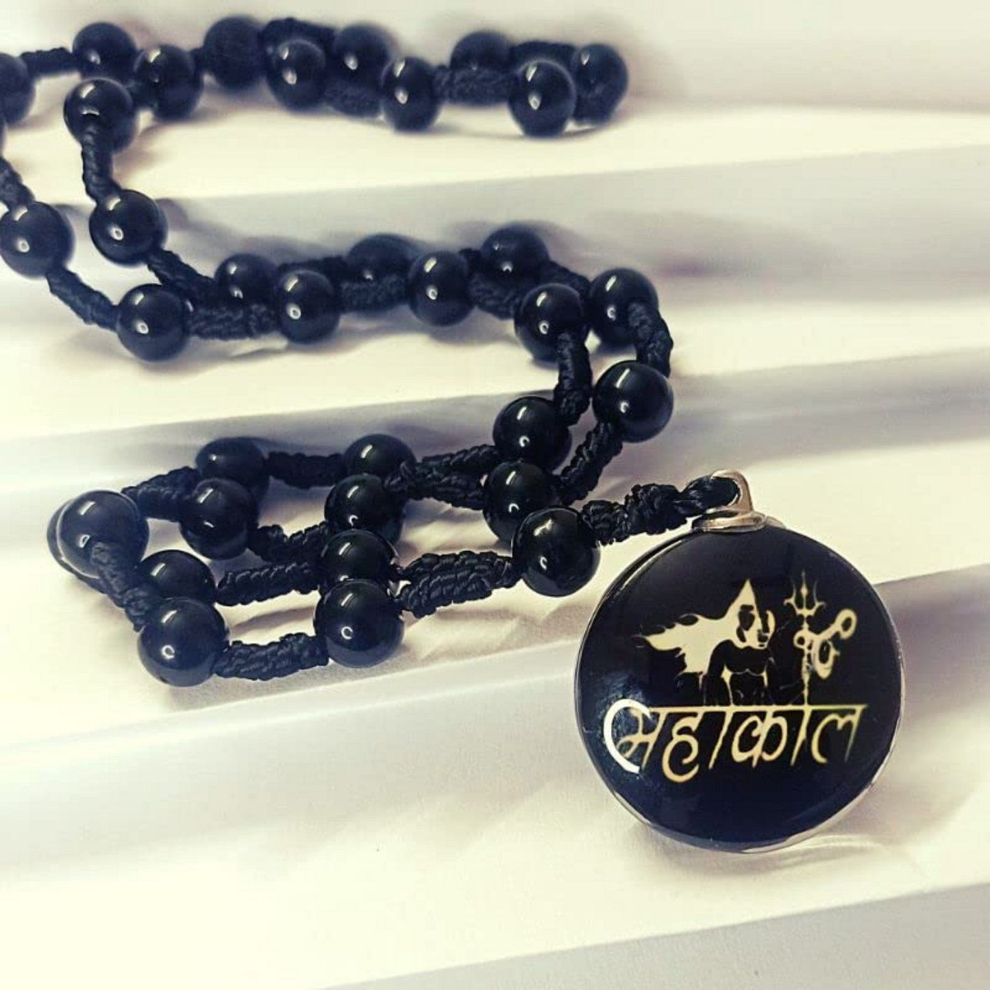 Black beaded necklace with a pendant featuring a design and text on a white background