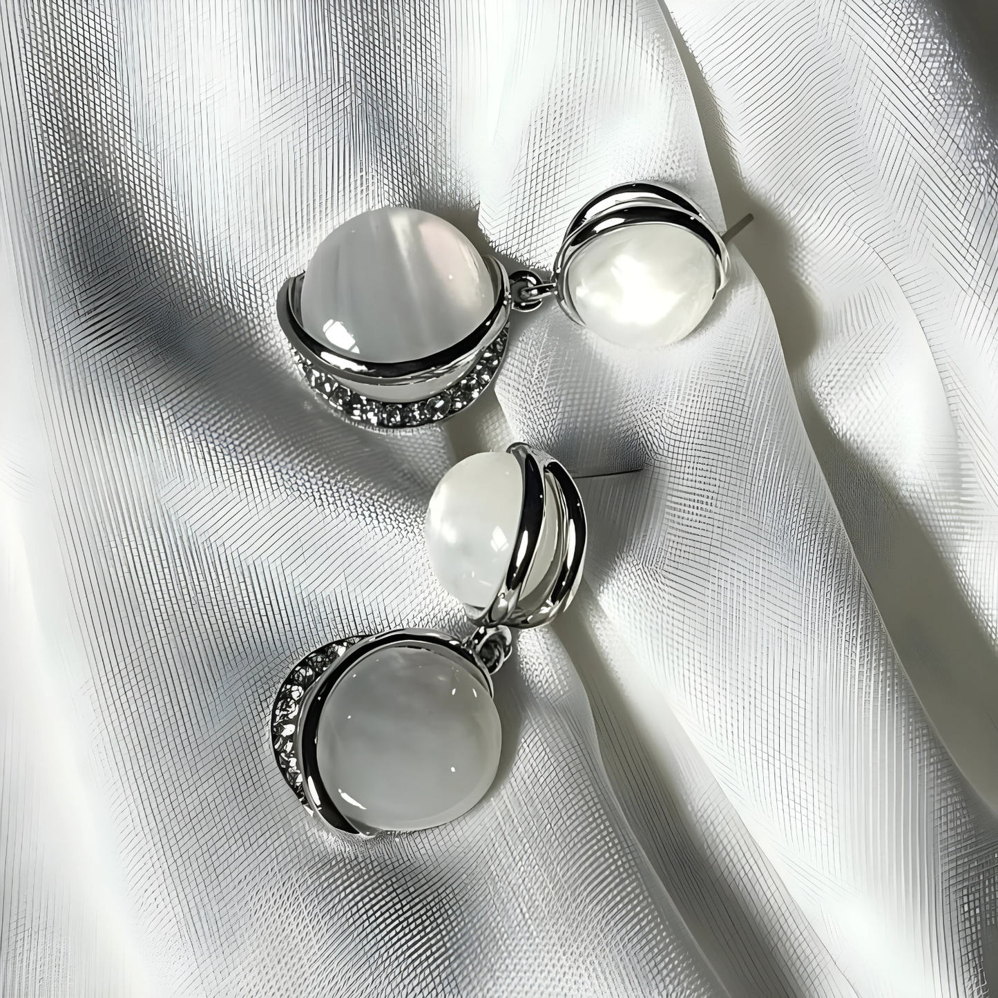 Pair of silver earrings with white stones on a white fabric background