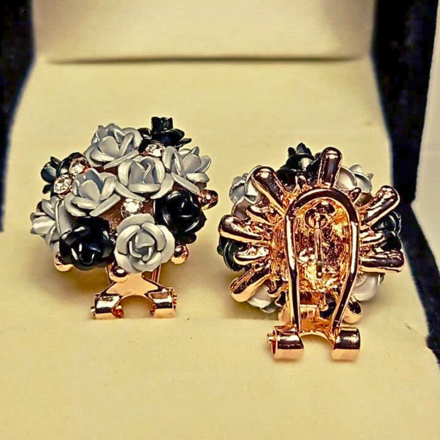 Pair of floral earrings with gold and black accents on a beige background