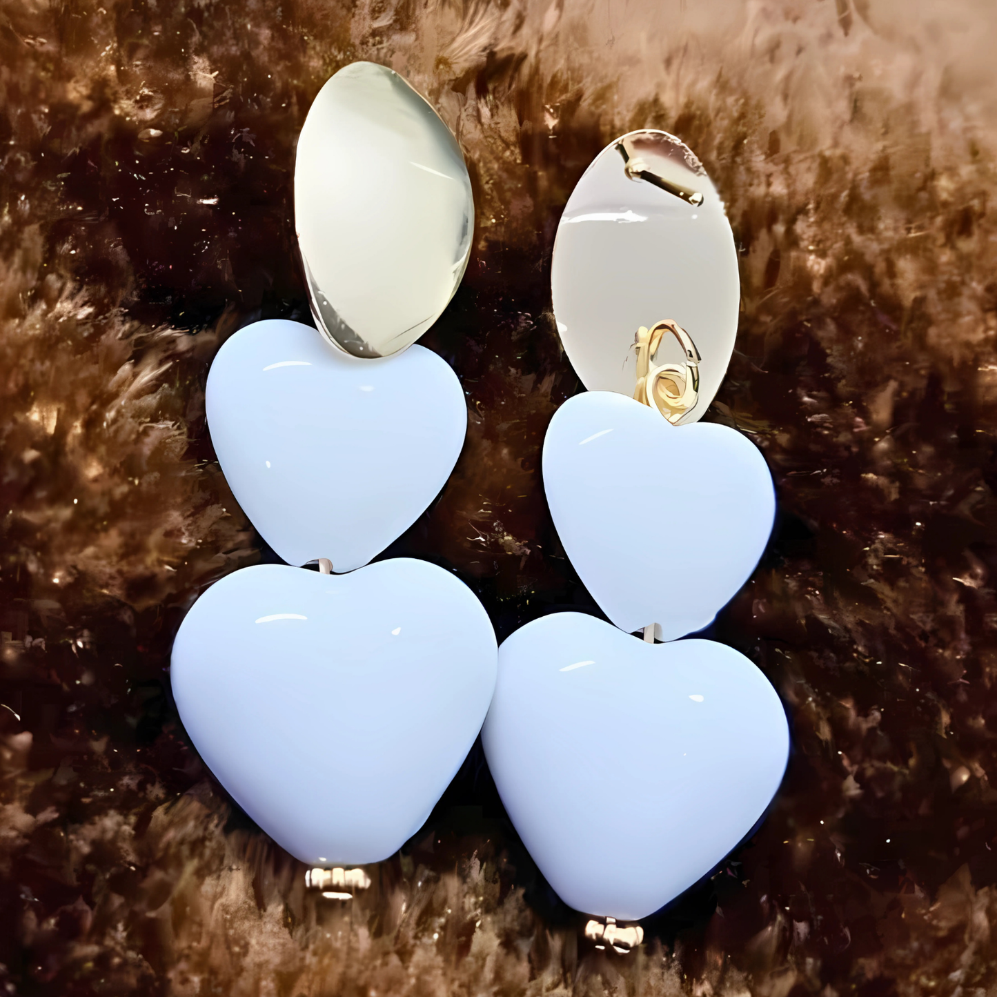 Pair of earrings with light blue heart-shaped stones and gold accents on a brown fur background