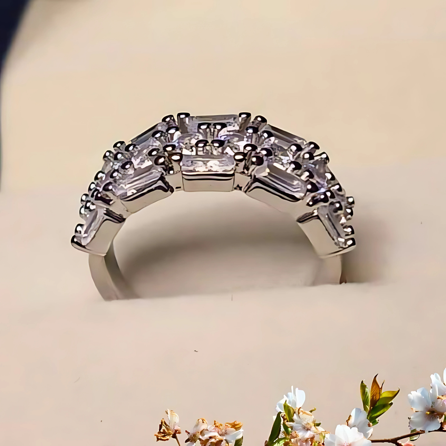 Silver ring with diamond accents on a beige surface with floral decorations.