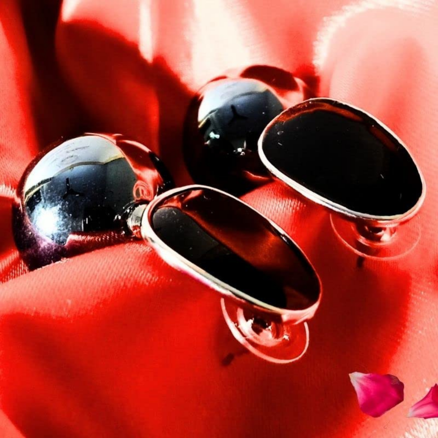 Pair of black oval earrings on a red surface with pink petals.