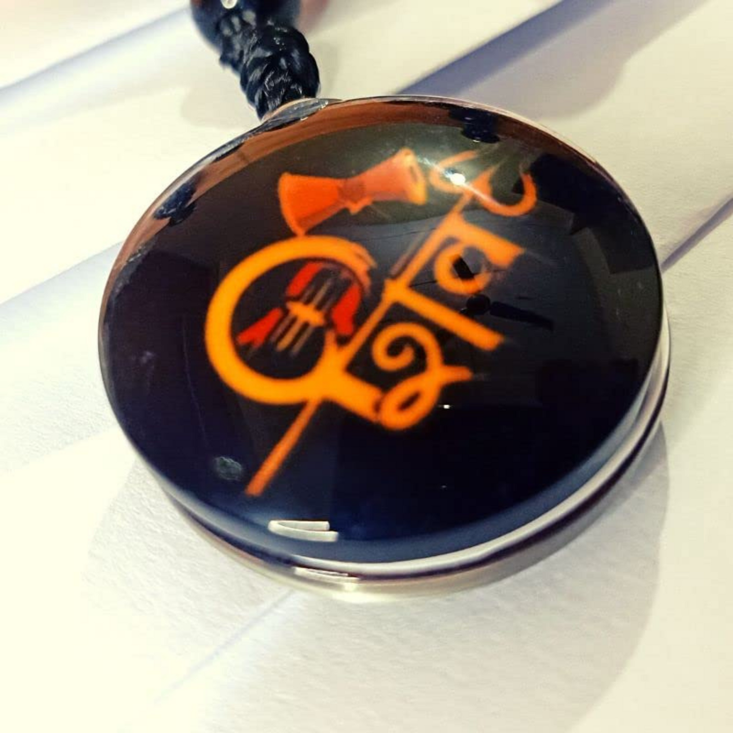 Round pendant with orange design on a black background, attached to a cord.
