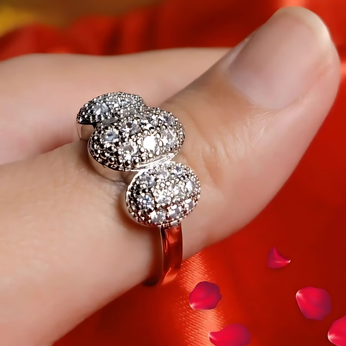 Silver ring with gemstones on a finger against a red background with rose petals.