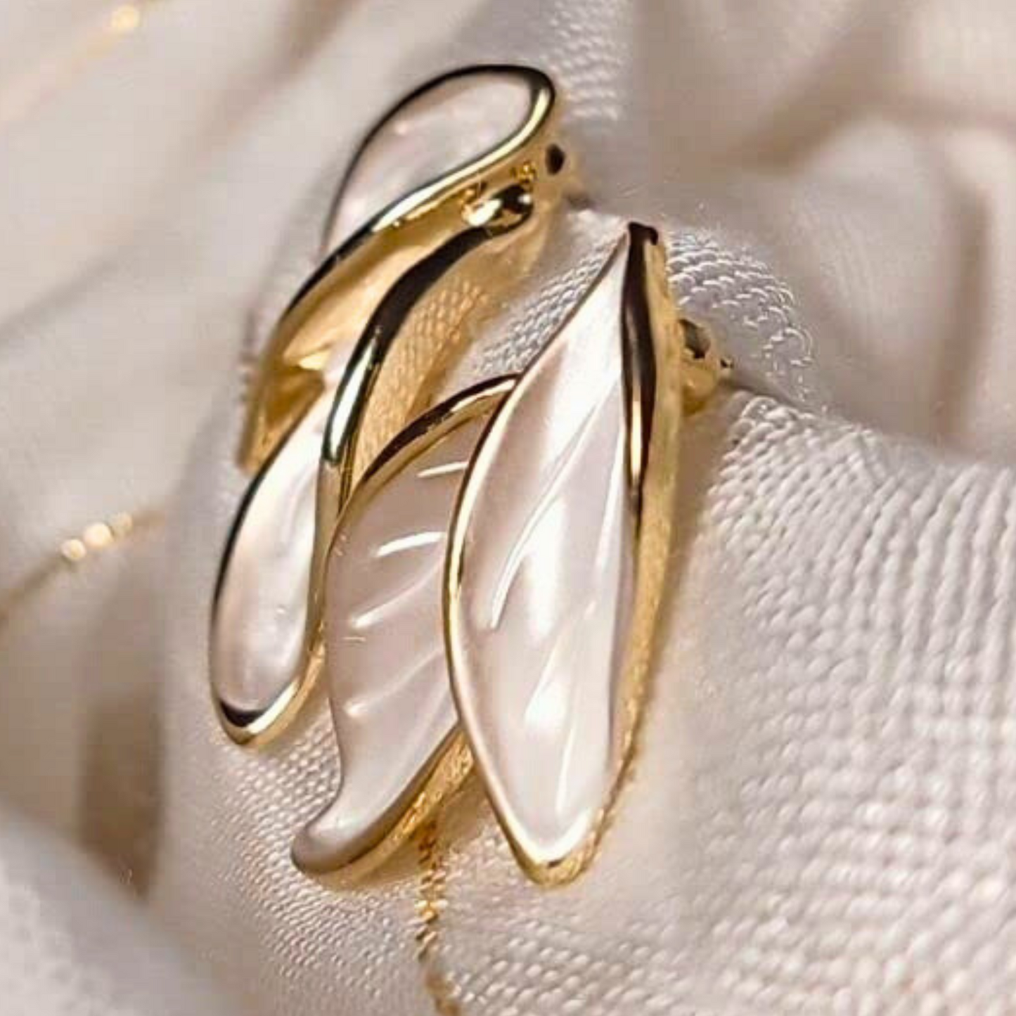 Gold and white earrings on a soft beige fabric background