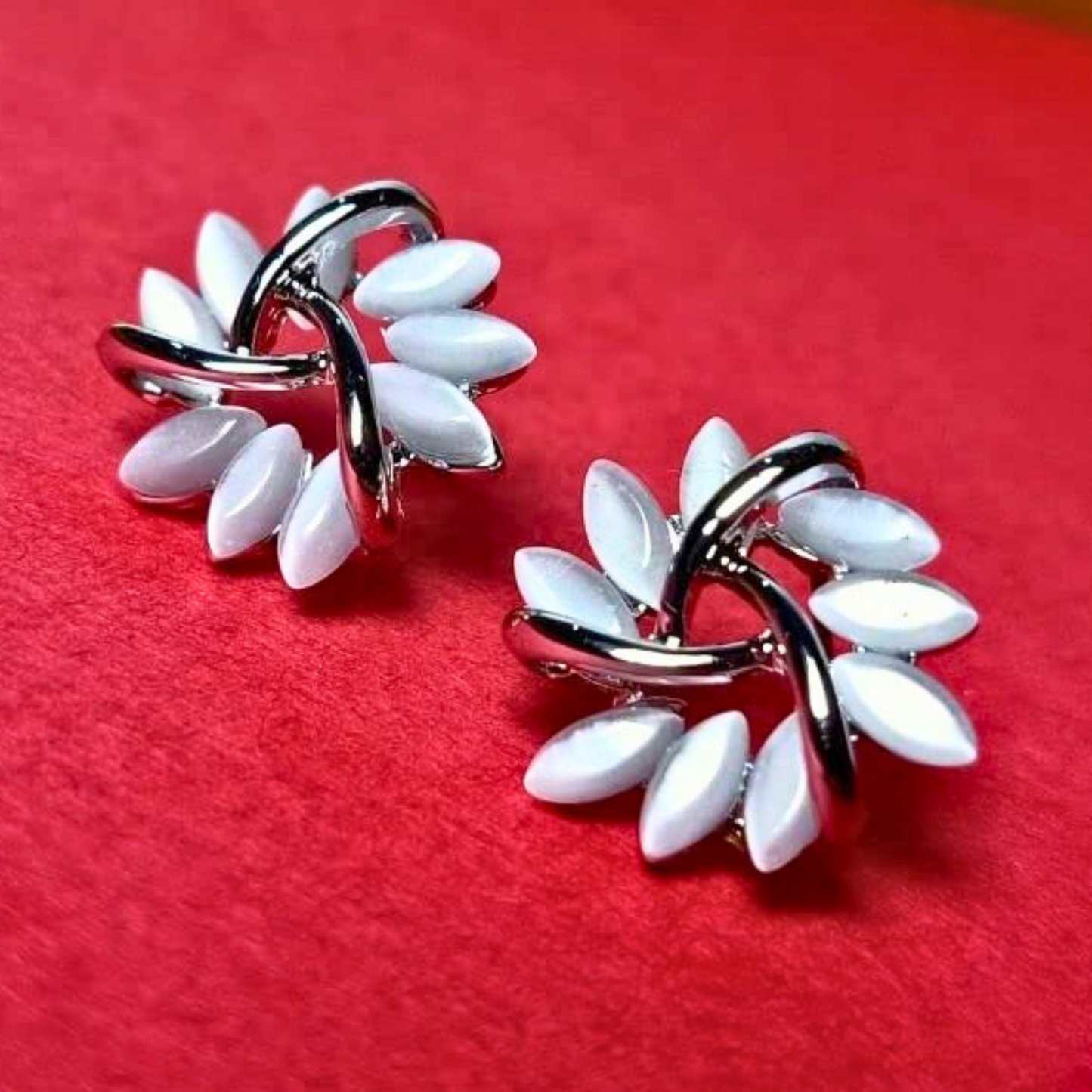 Pair of silver and white leaf-shaped earrings on a red background