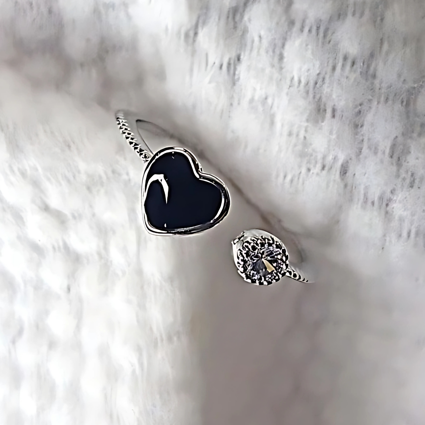 Silver ring with black heart-shaped stone on a textured white surface