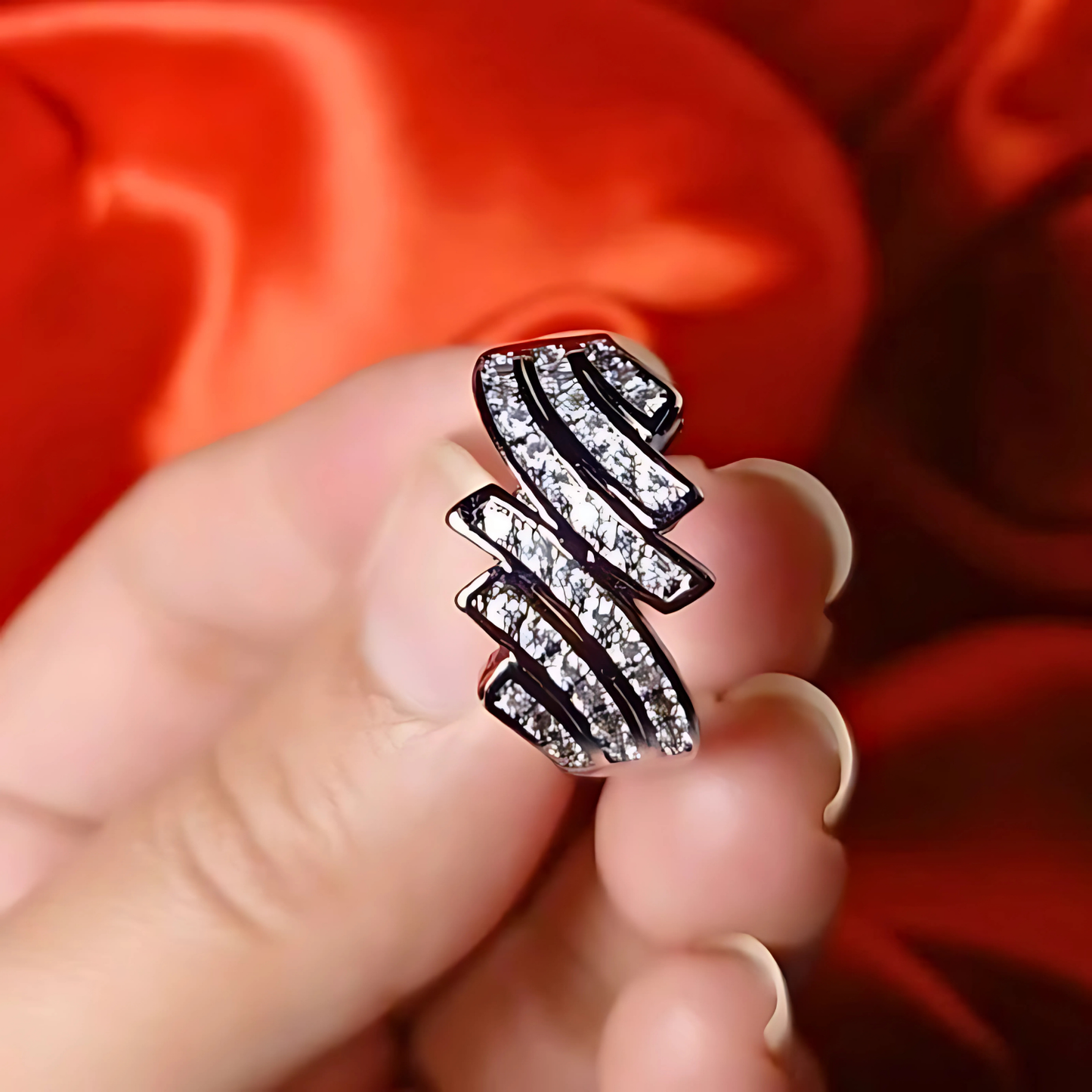 Silver ring with gemstones held in a hand against a red fabric background