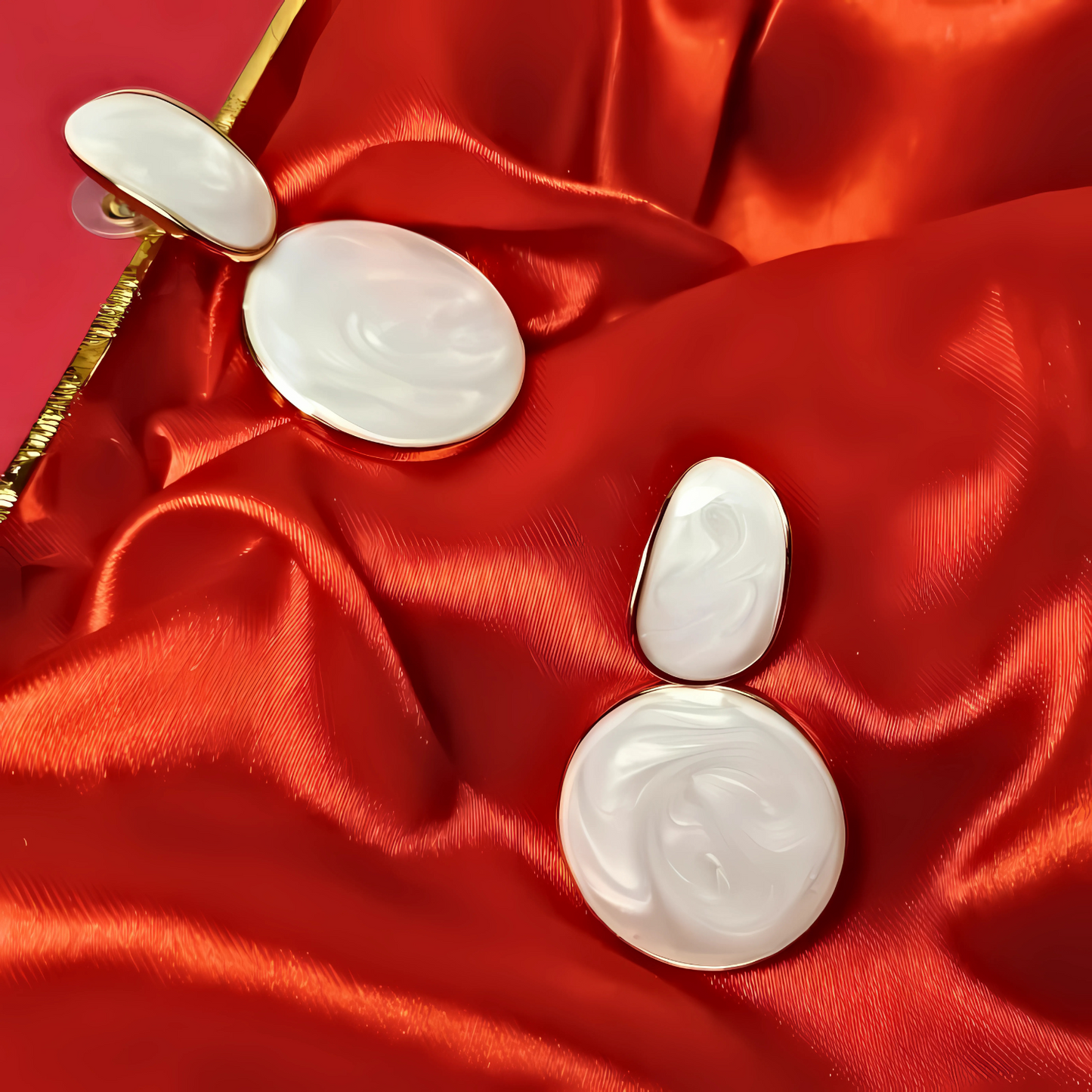 Pair of white earrings on a red satin surface