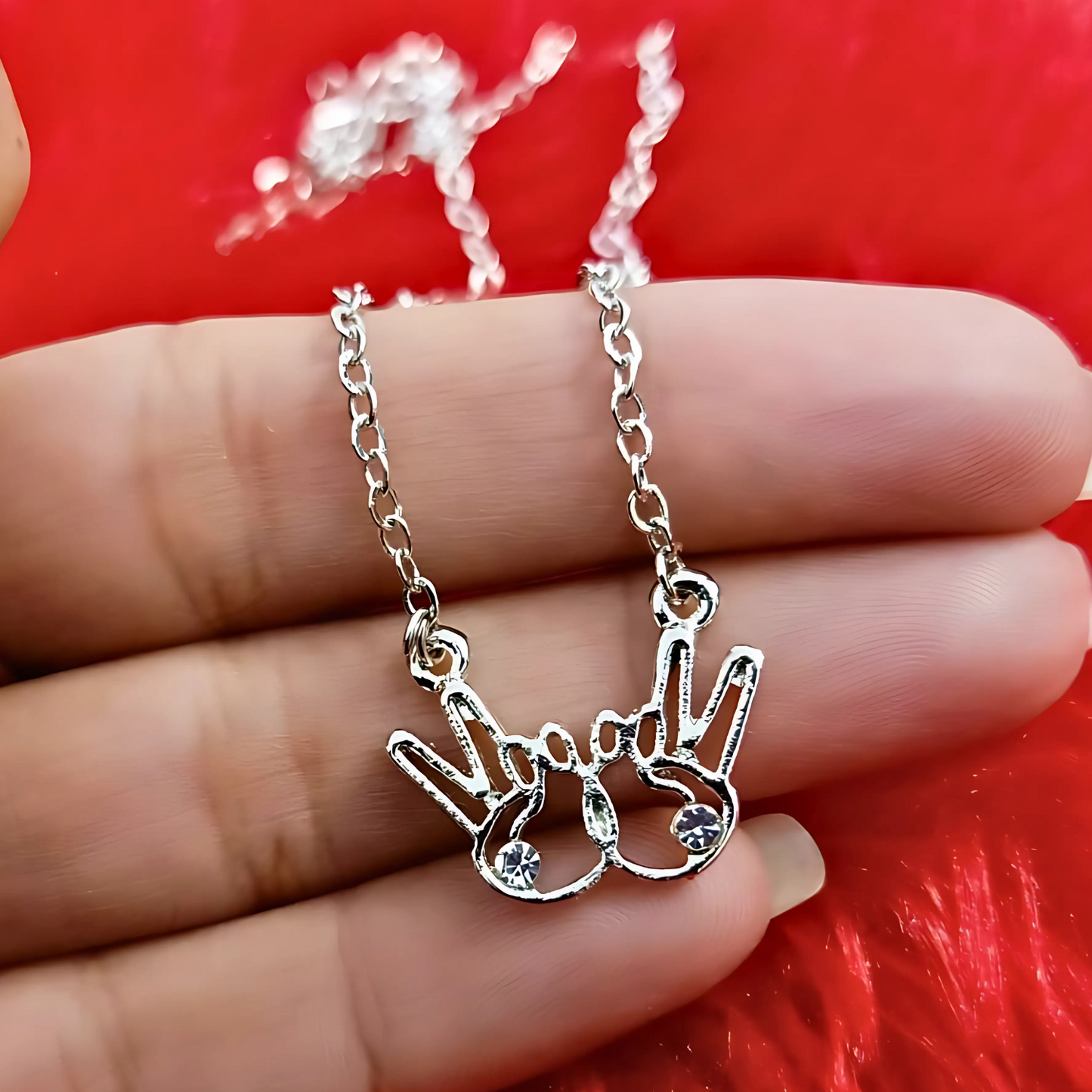 Silver necklace with a hand-shaped pendant held between fingers against a red background