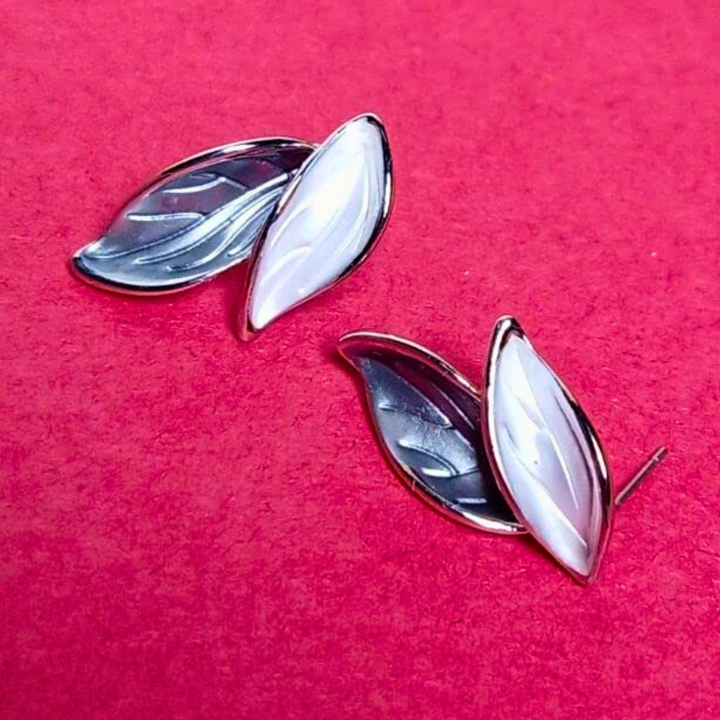 Pair of silver leaf-shaped earrings on a pink background