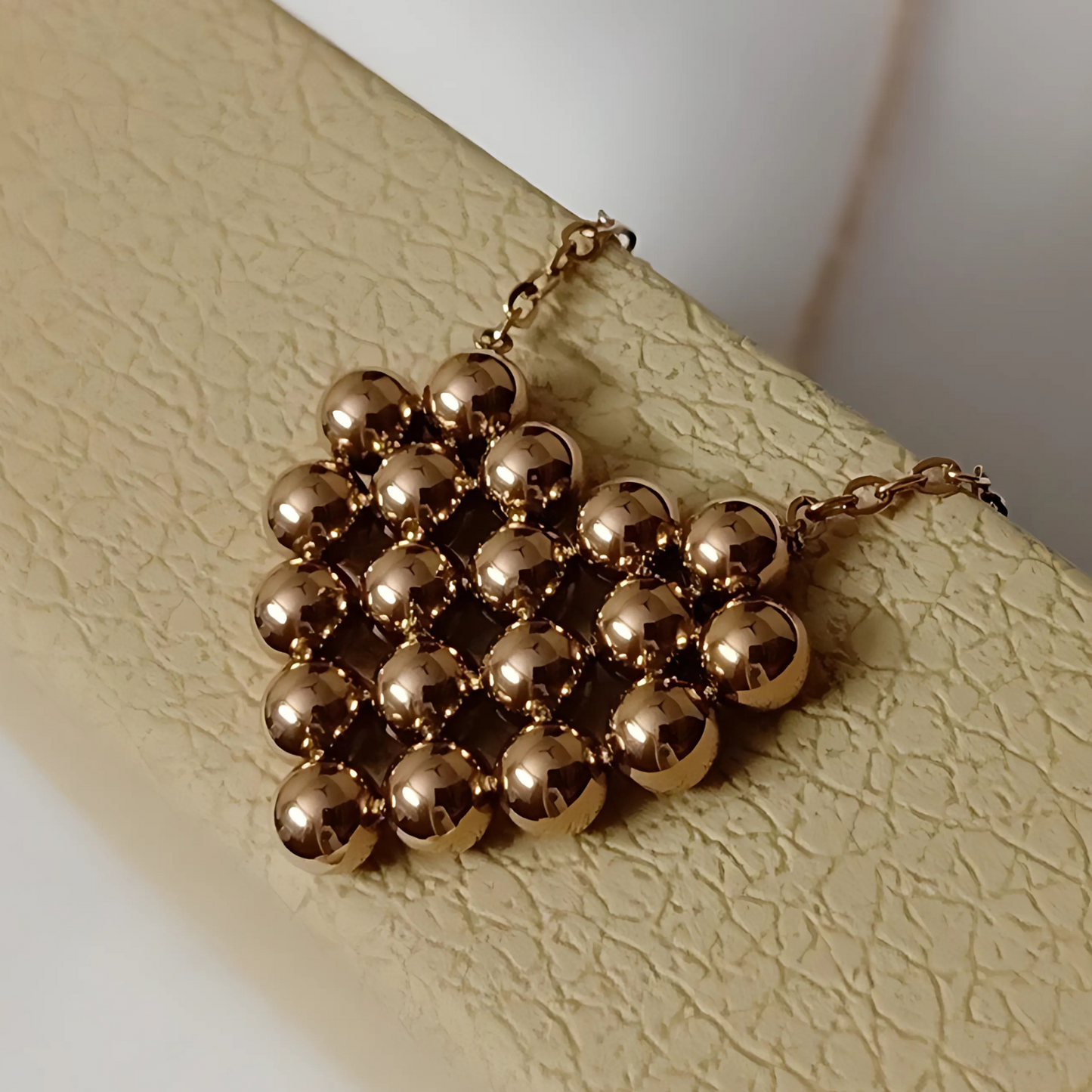 Gold beaded necklace on a textured beige surface