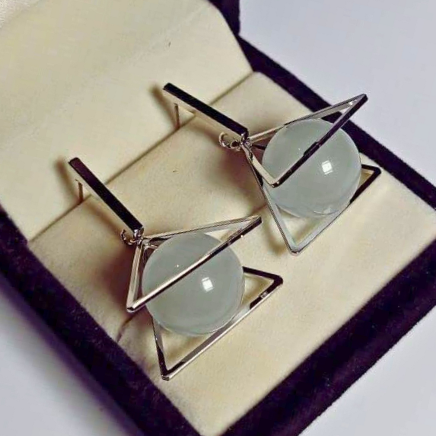 Pair of earrings with geometric design on a purple cushioned jewelry box.