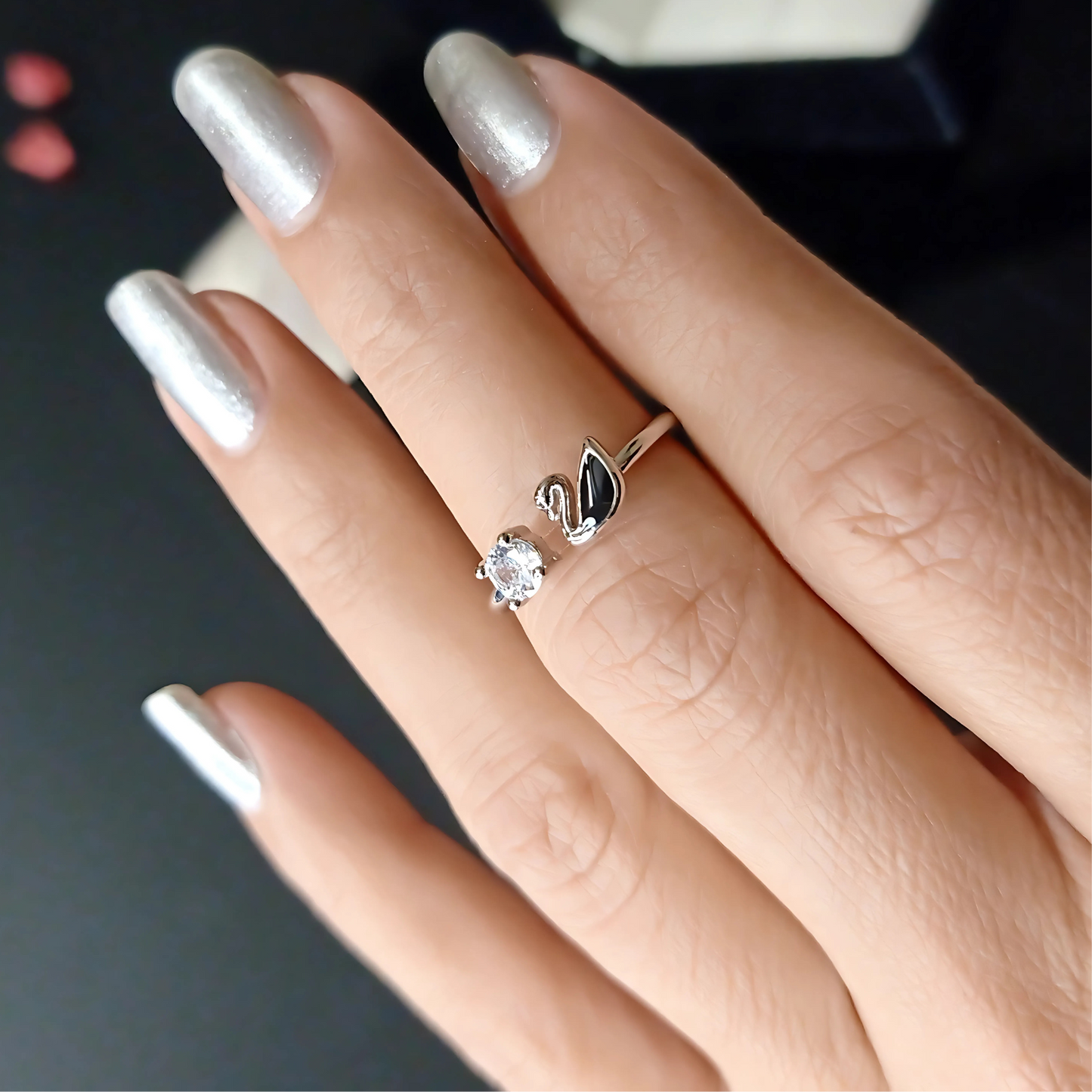 Silver swan-shaped ring on a finger with silver nail polish.