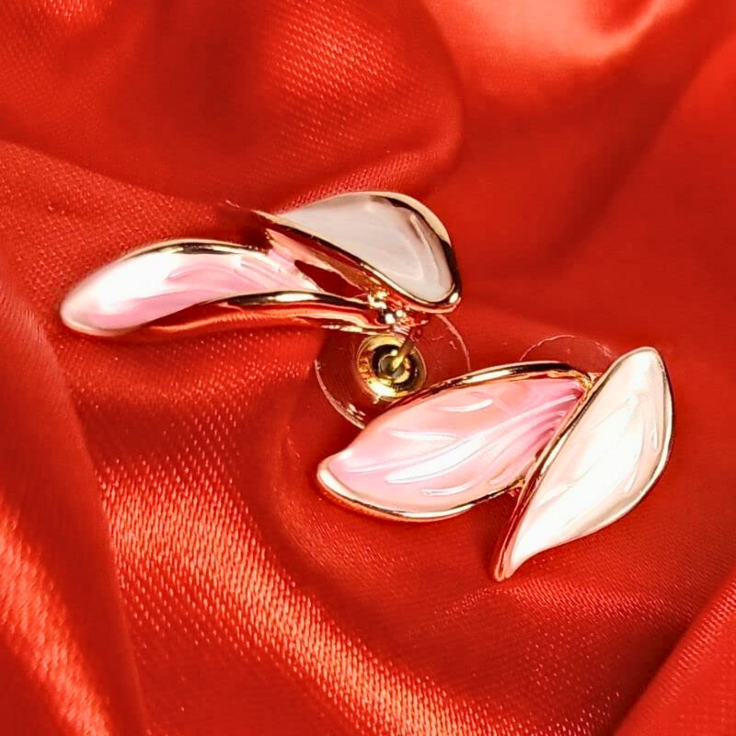 Pink and gold leaf-shaped earrings on red fabric