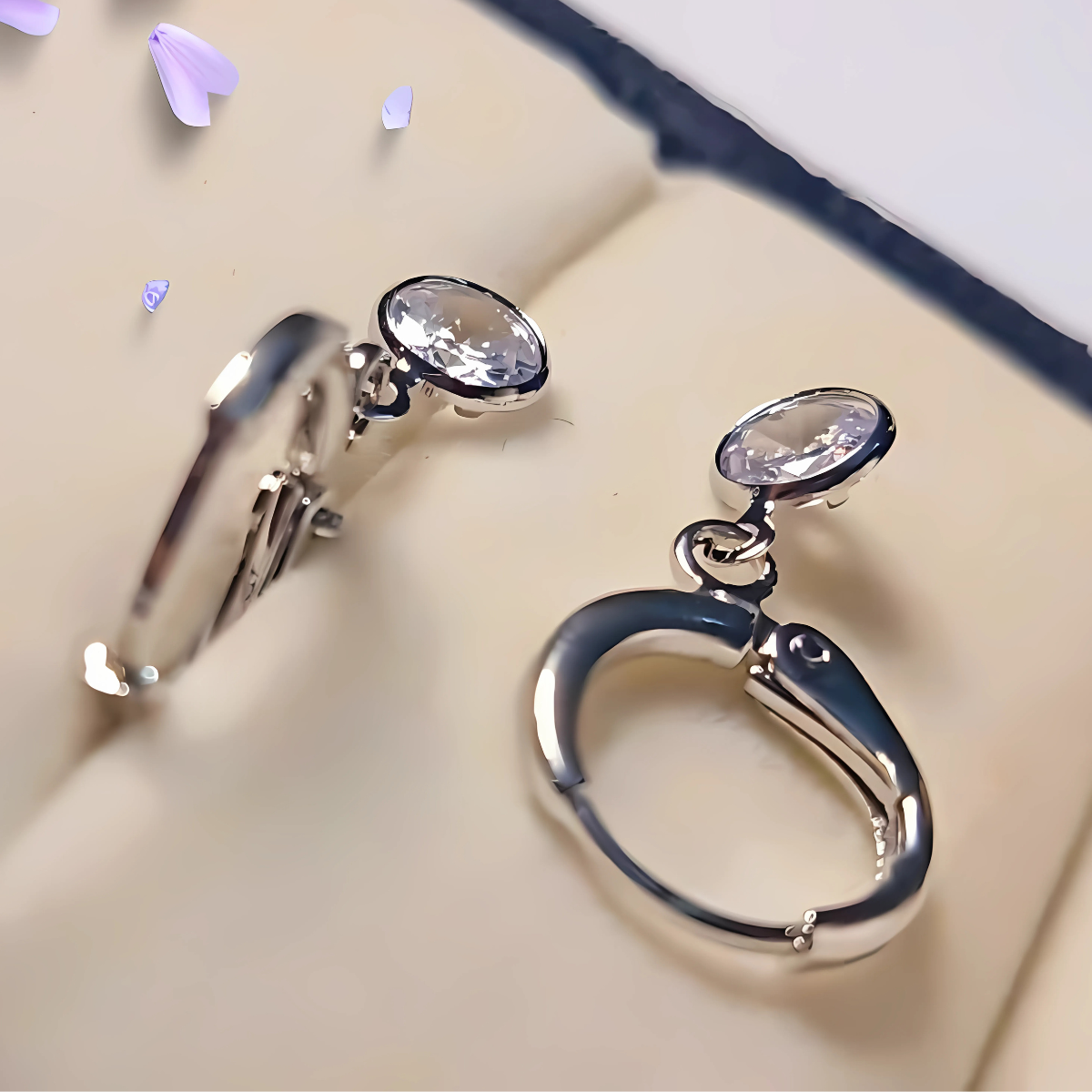 Silver earrings with clear gemstones on a beige surface