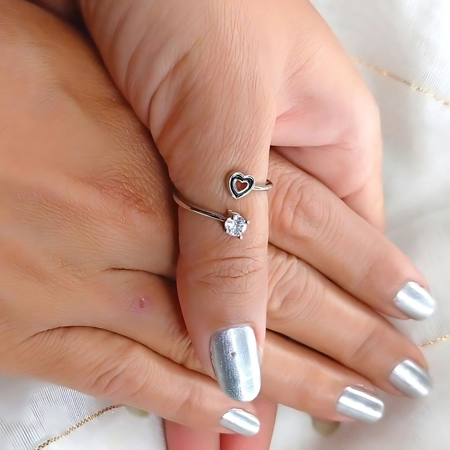 Close-up of a hand wearing two silver rings with heart designs on a light background.