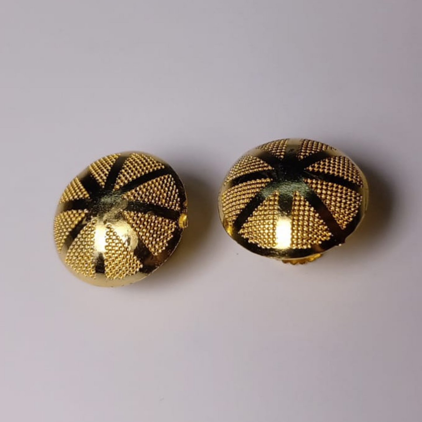 Pair of gold earrings with black pattern on a light gray background