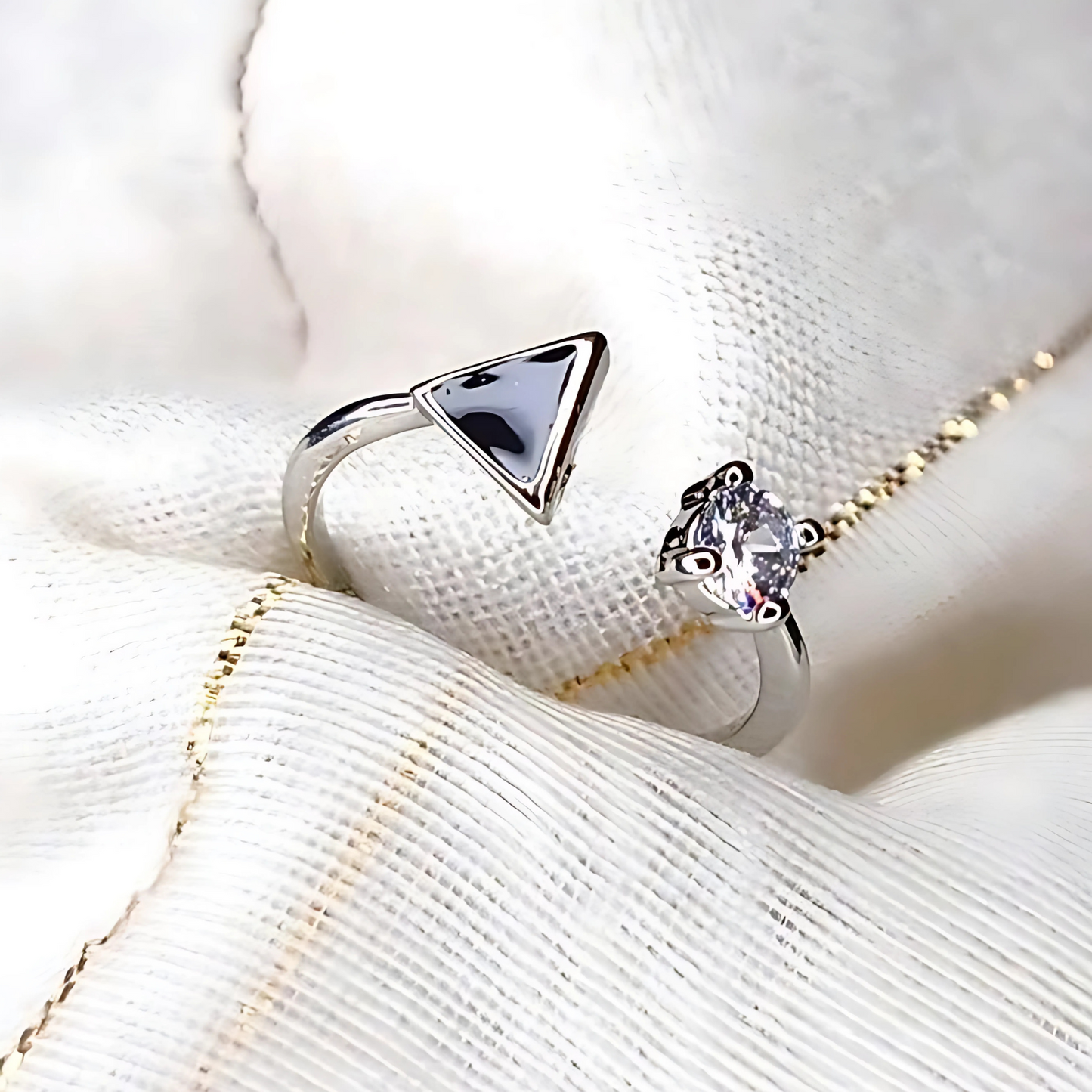 Two silver rings, one triangle-shaped and one with a heart-shaped gem, on a textured white surface.