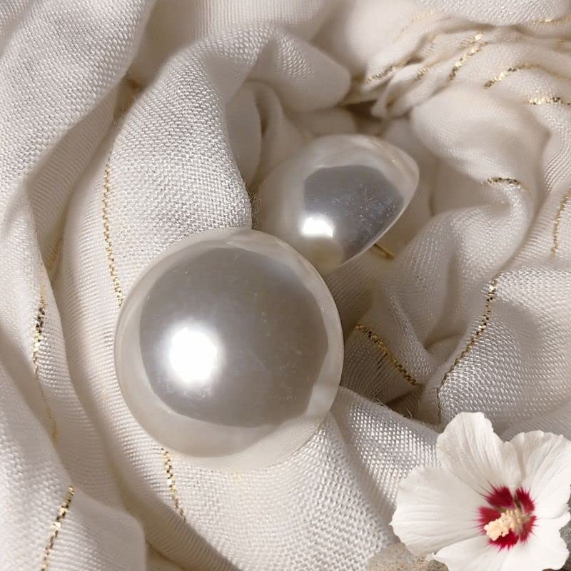 Pearl earrings on a textured white fabric background with a small flower.